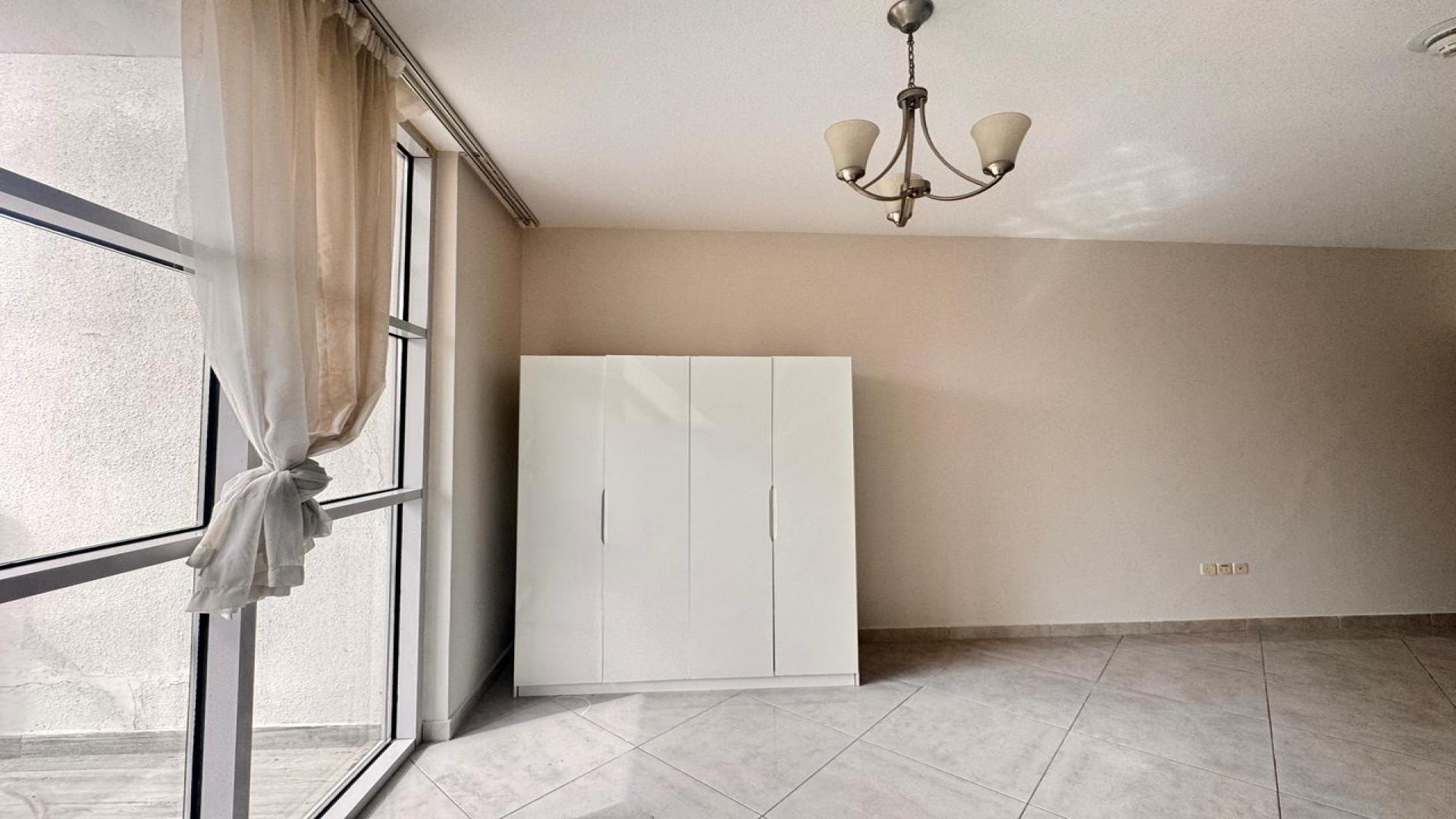 Studio apartment interior in Chaimaa Premiere, Jumeirah Village Circle, featuring large window and wardrobe