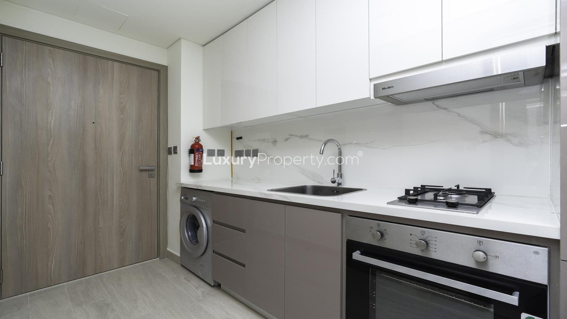 "Modern Meydan One studio apartment interior with wood flooring and built-in wardrobe.",Modern studio kitchen in Meydan One apartment with sleek appliances and marble backsplash