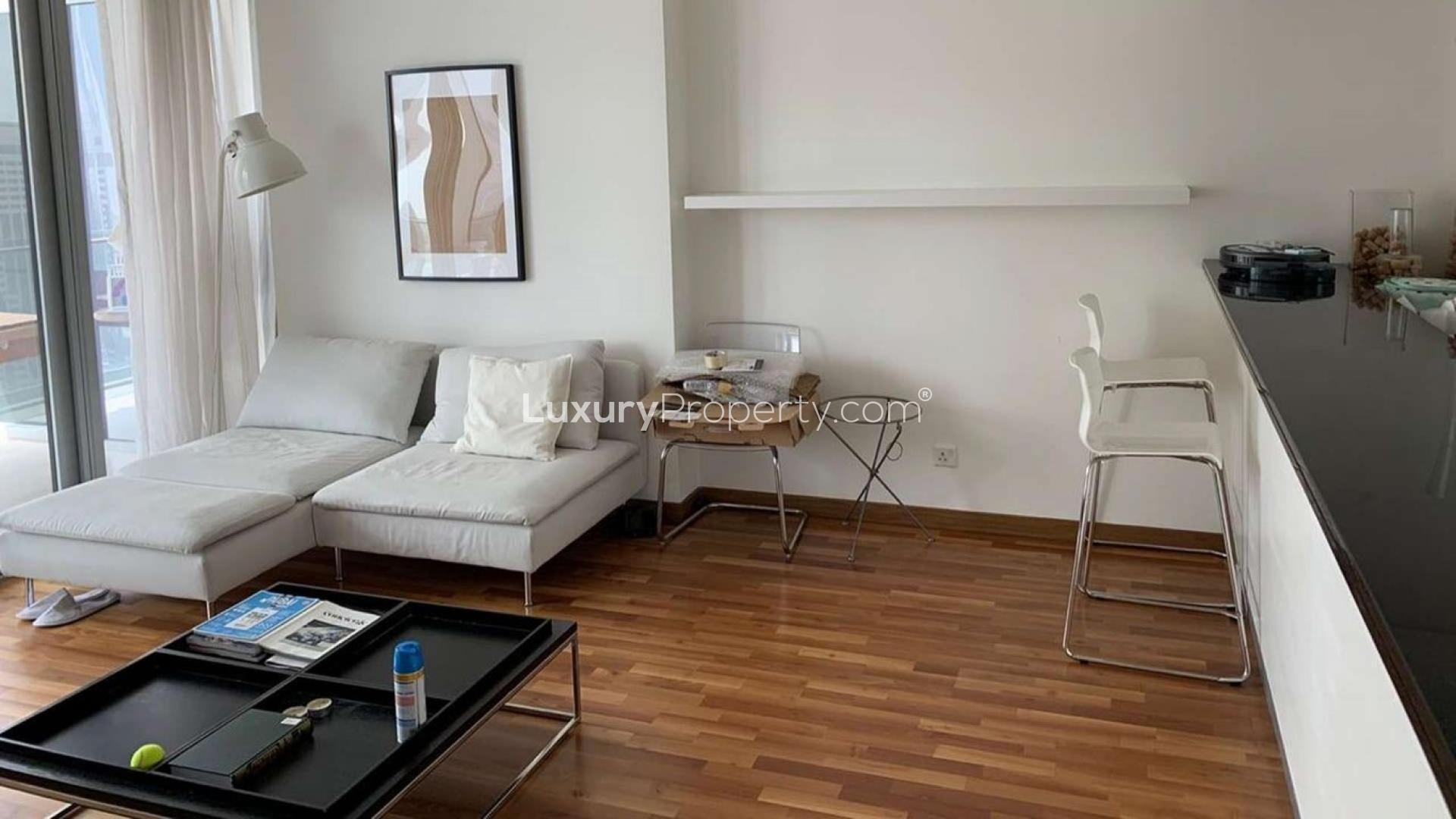 "Burj Daman apartment exterior with glass balconies, overlooking DIFC skyline, sunny day view.",Modern living room in Burj Daman apartment, featuring sleek furniture and natural light