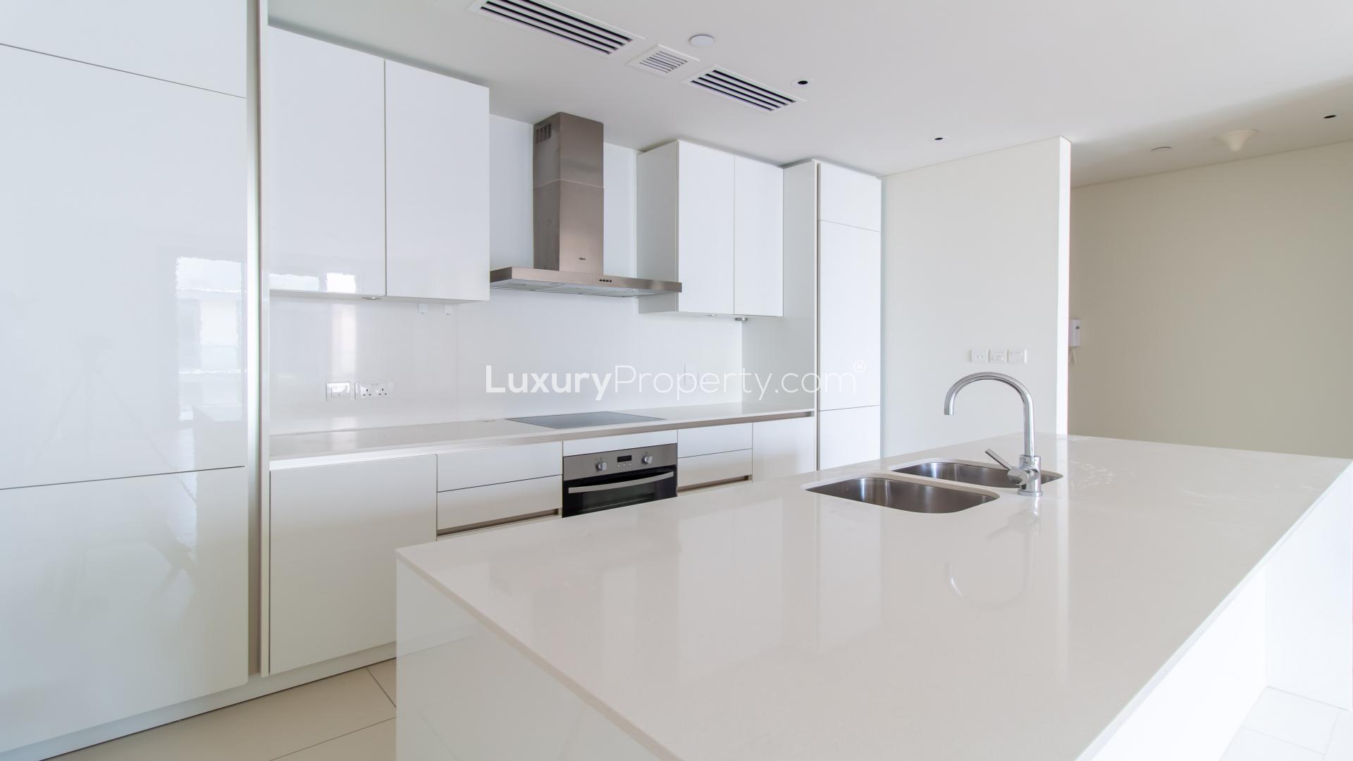 "Spacious balcony with modern glass railing in City Walk, Dubai apartment for rent.",Modern kitchen in 1-bedroom City Walk apartment, Dubai, with sleek white cabinetry and island