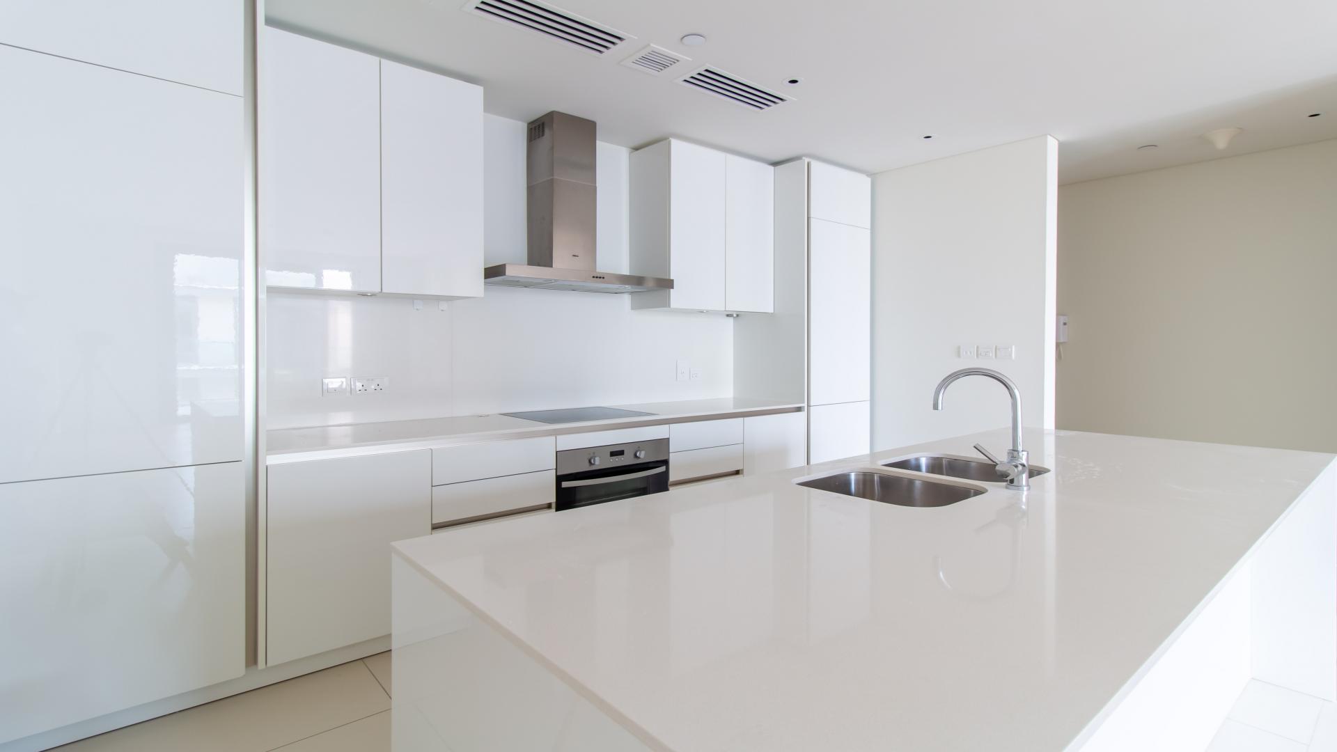 "Spacious balcony with modern glass railing in City Walk, Dubai apartment for rent.",Modern kitchen in 1-bedroom City Walk apartment, Dubai, with sleek white cabinetry and island