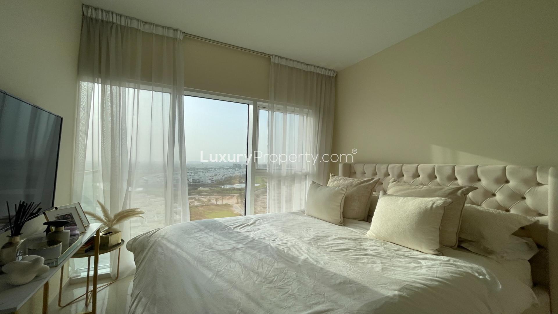 Bedroom with large window, TV, and city view in Damac Hills Golf Vita apartment