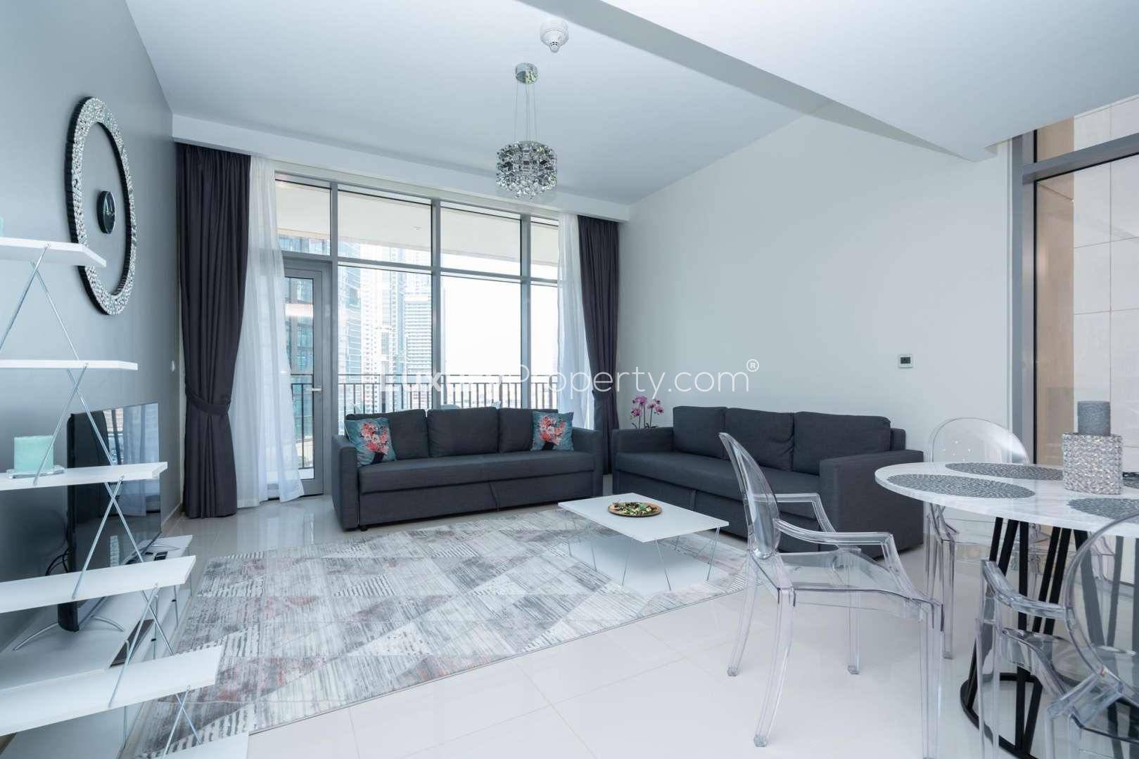 Alt text: "Downtown Dubai apartment view, poolside with skyscrapers, BLVD Crescent, for rent.",Furnished living room in Boulevard Crescent apartment, Downtown Dubai, with modern decor and balcony view