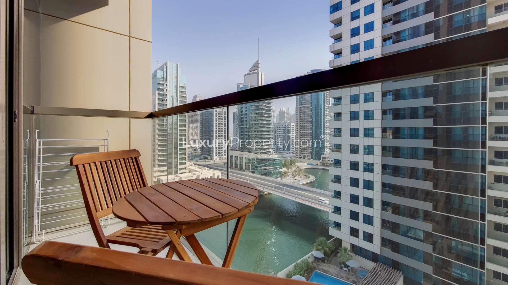 "Modern high-rise buildings in Dubai Marina's No.9 community, waterfront view, palm trees, cityscape.",Balcony view of Dubai Marina from No.9 apartment with wooden furniture and skyscrapers