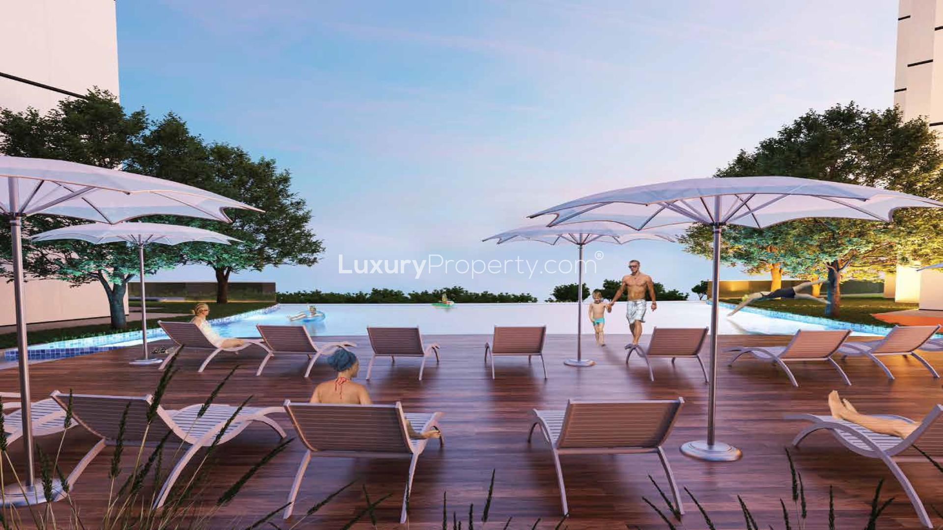 Outdoor pool area with lounge chairs at Maimoon Gardens, Jumeirah Village Circle apartment