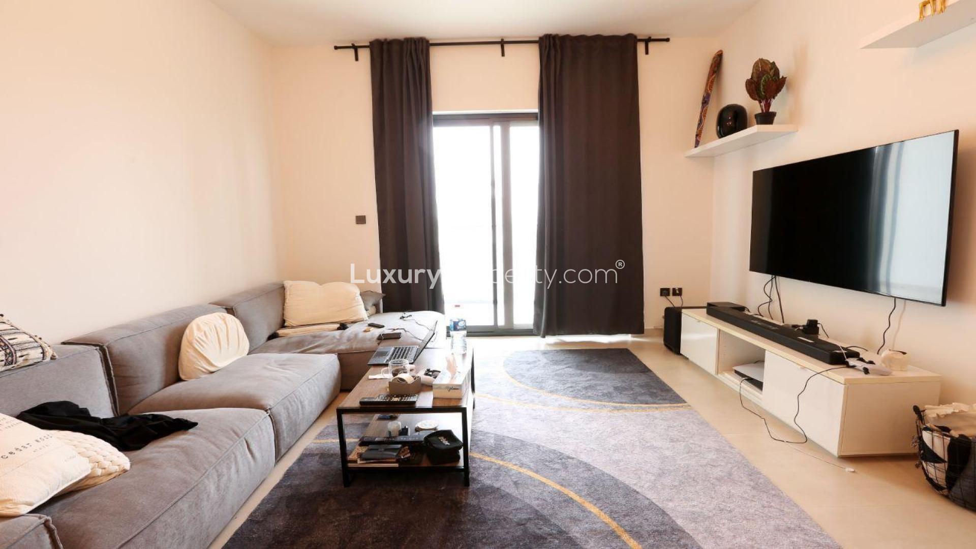 N/A,Modern living room in JVC apartment for sale, featuring cozy gray sofa and large TV