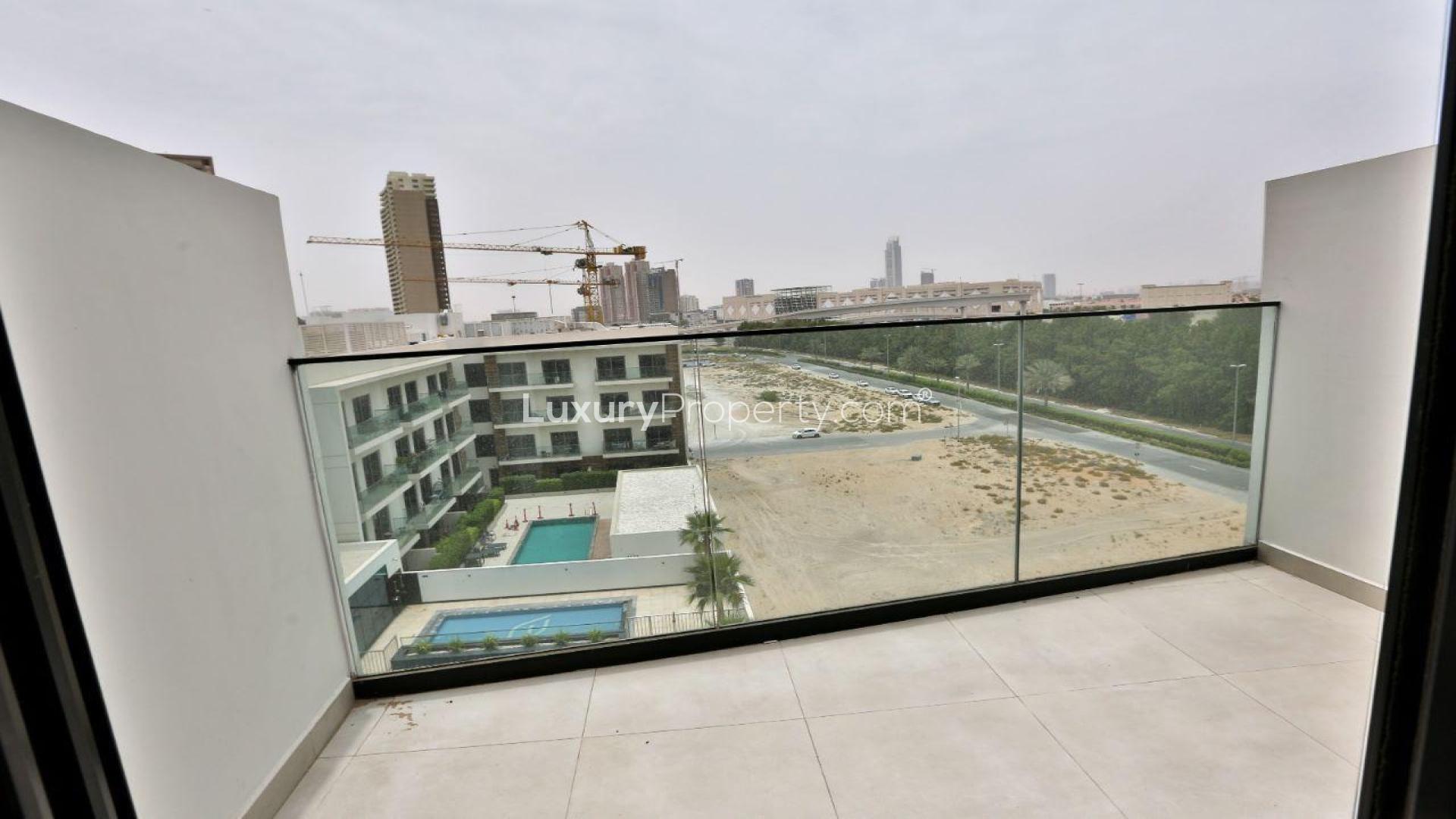 "Balcony view from JVC apartment for sale, overlooking pool and construction cranes.",Modern living room in JVC apartment for sale, featuring cozy seating and open kitchen