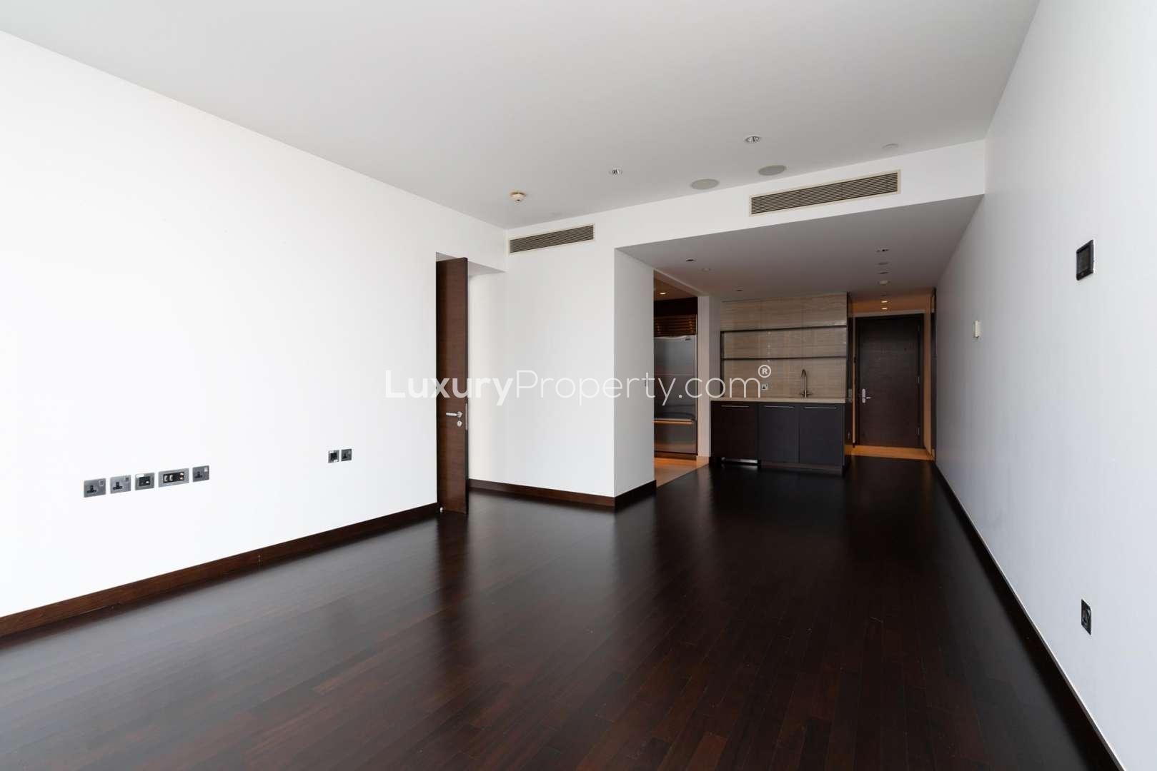 Empty living area in luxury Downtown Dubai apartment with dark wood flooring and modern kitchen