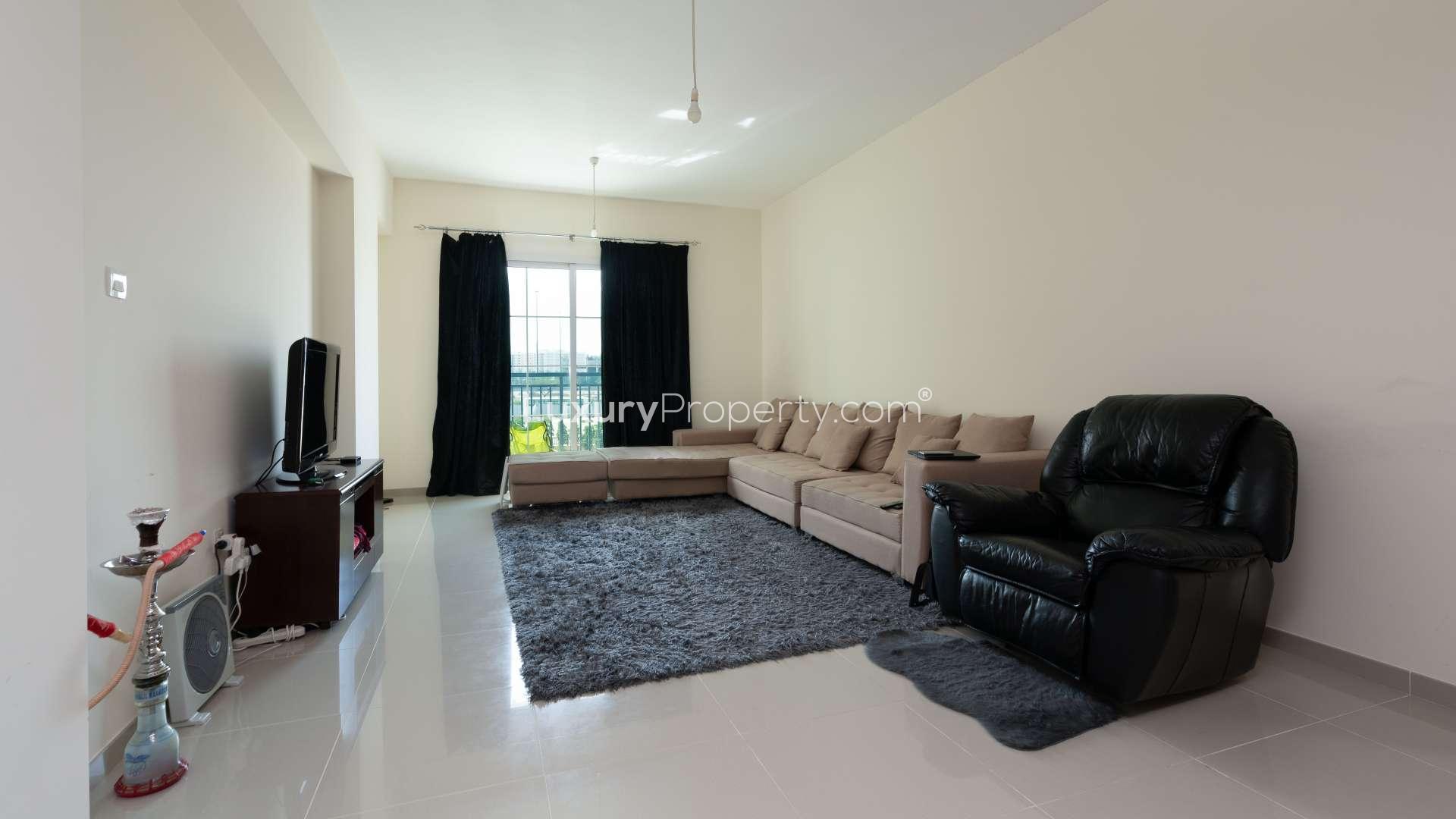 Living room with sectional sofa, armchair, and TV in Jumeirah Village Triangle apartment