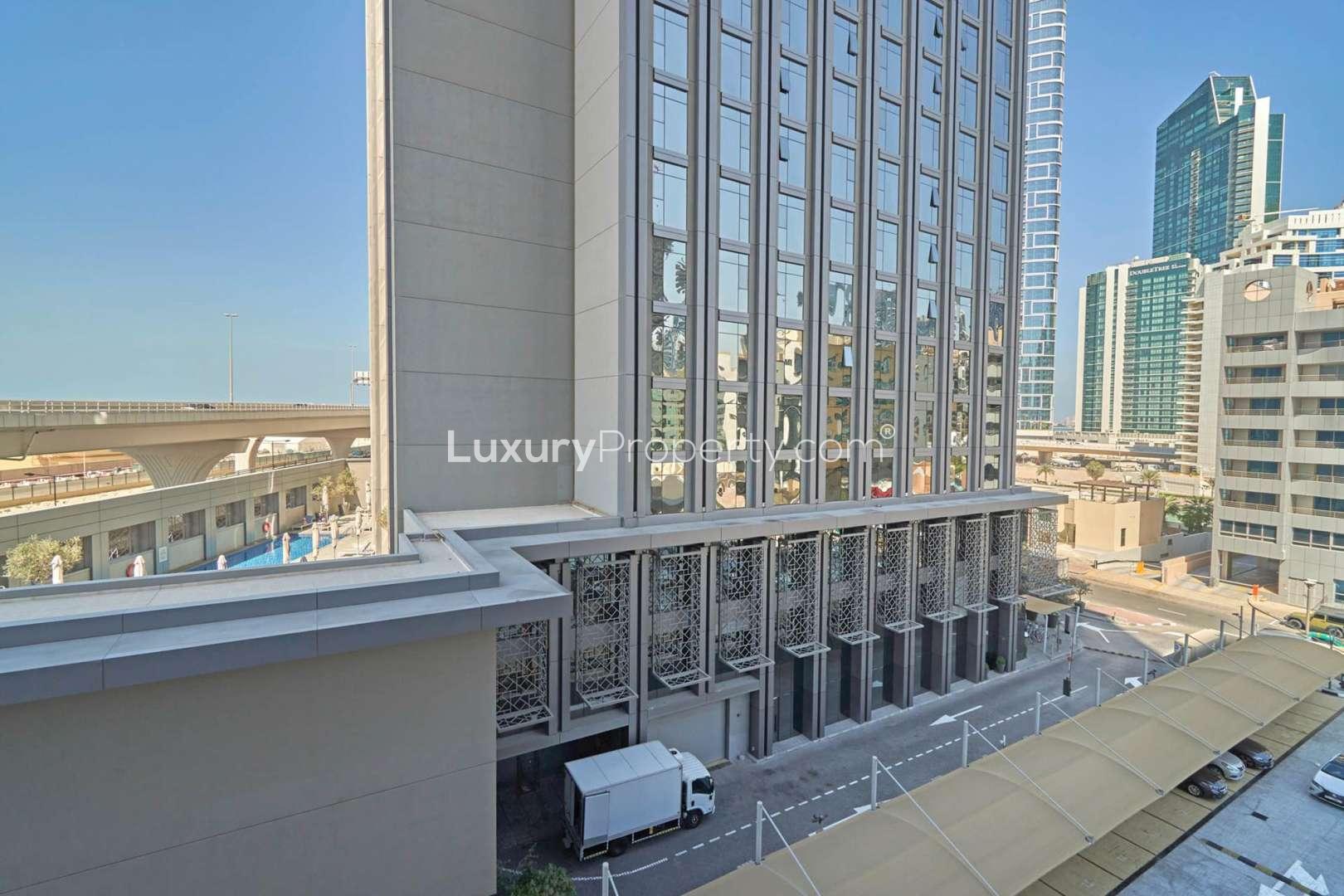 "Balcony view from luxury hotel room in TFG Marina Hotel, Dubai Marina for sale.","Exterior view of TFG Marina Hotel in Dubai Marina, showcasing modern architecture and surroundings.",Luxury one-bedroom apartment interior at TFG Marina Hotel, Dubai Marina for sale