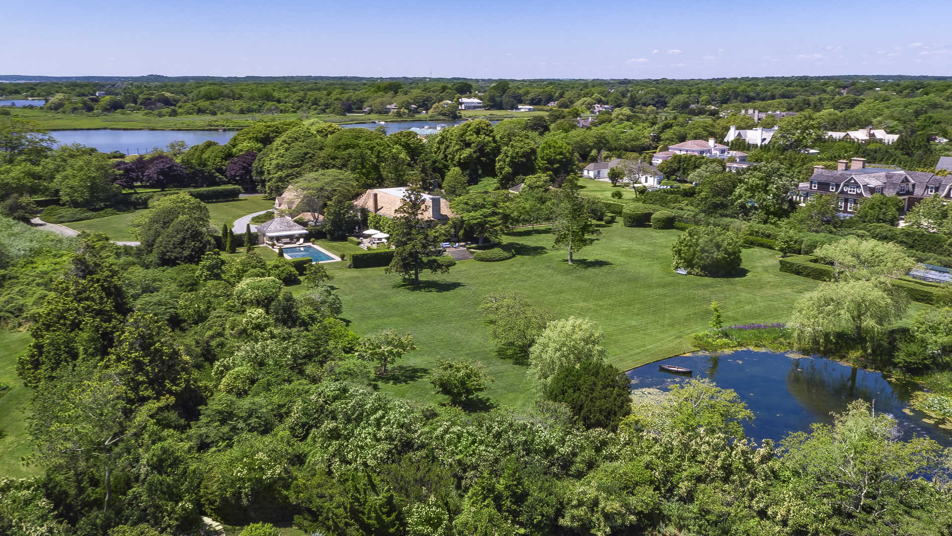 "French-style villa entrance with tree-lined driveway in Southampton, Hamptons, New York.",Aerial view of luxurious French-style villa with pool in Southampton's Hamptons community