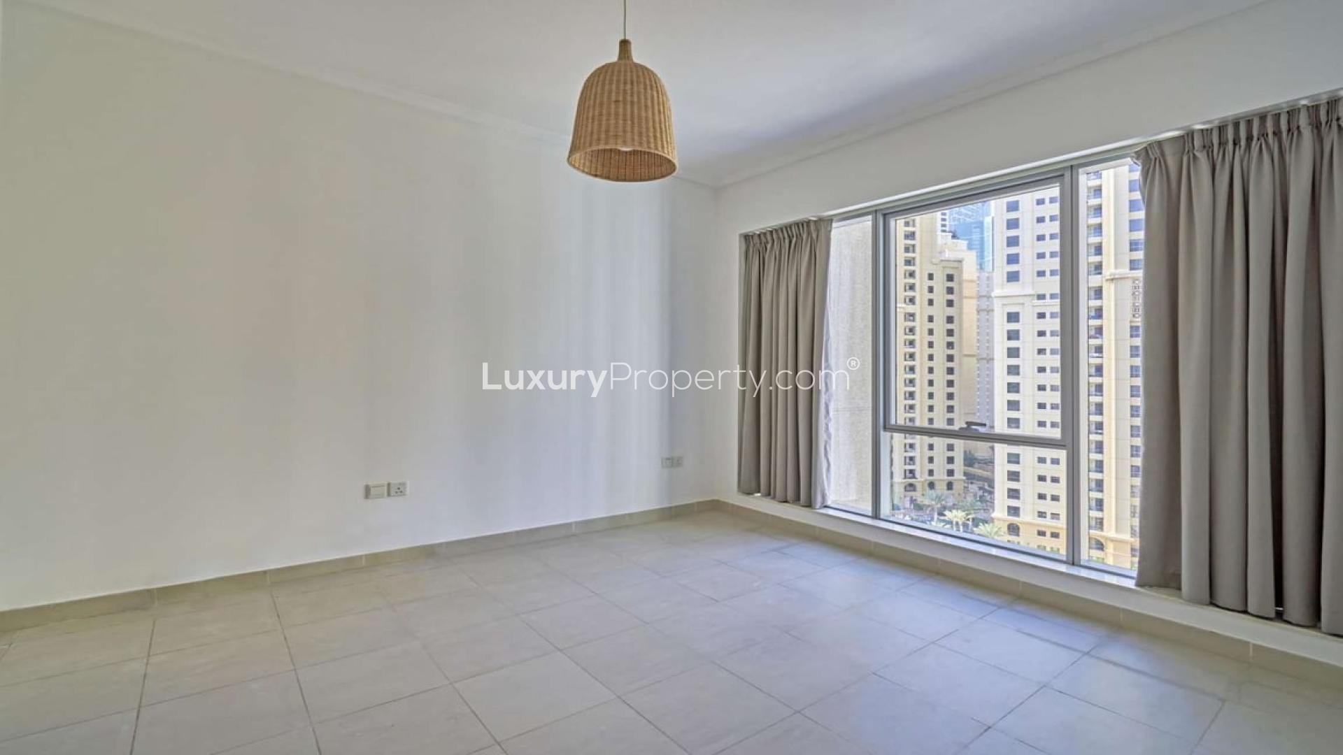 "Bright living area in 2-bedroom apartment with marina views, Dubai Marina, for rent.",Empty room with large window and city views in Dubai Marina apartment for rent