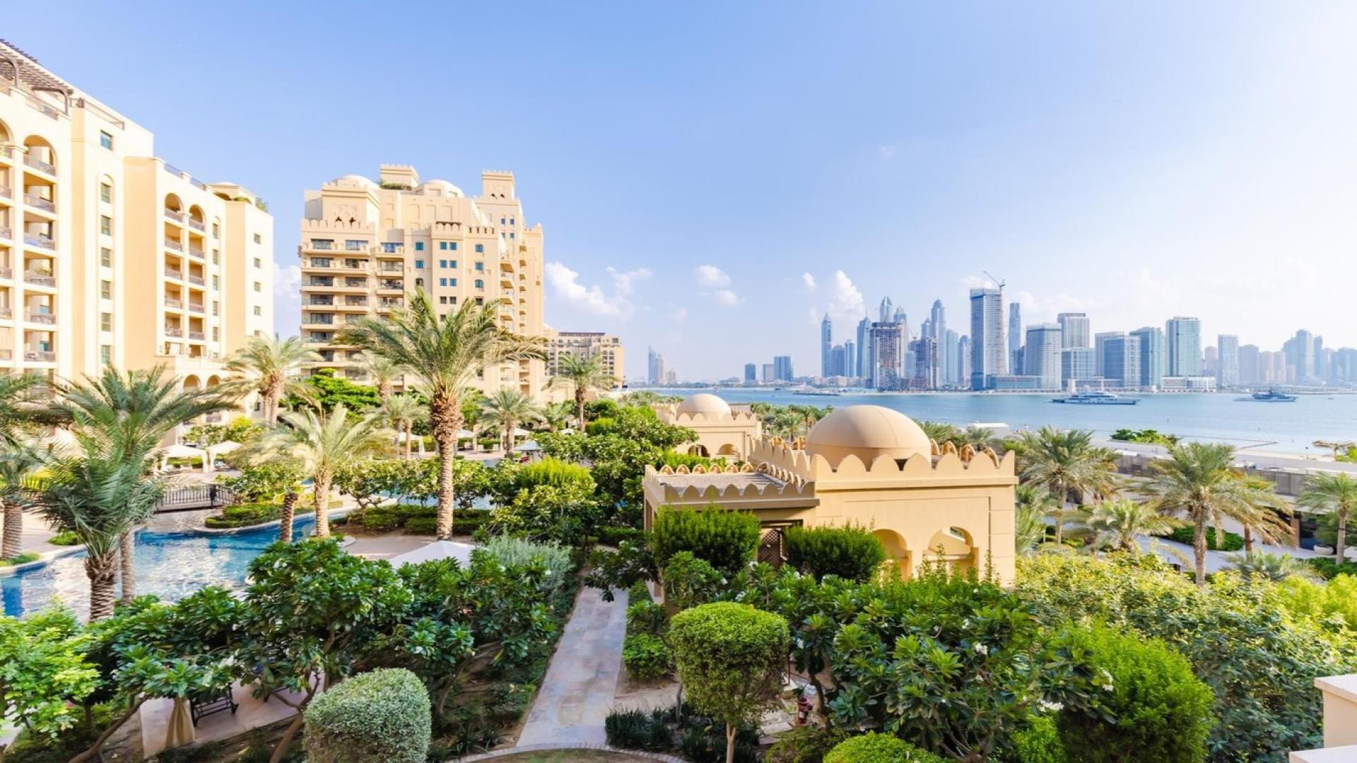 "Bright Palm Jumeirah apartment interior with modern kitchen and spacious living area views.",Palm Jumeirah apartment view with lush gardens and city skyline in the background