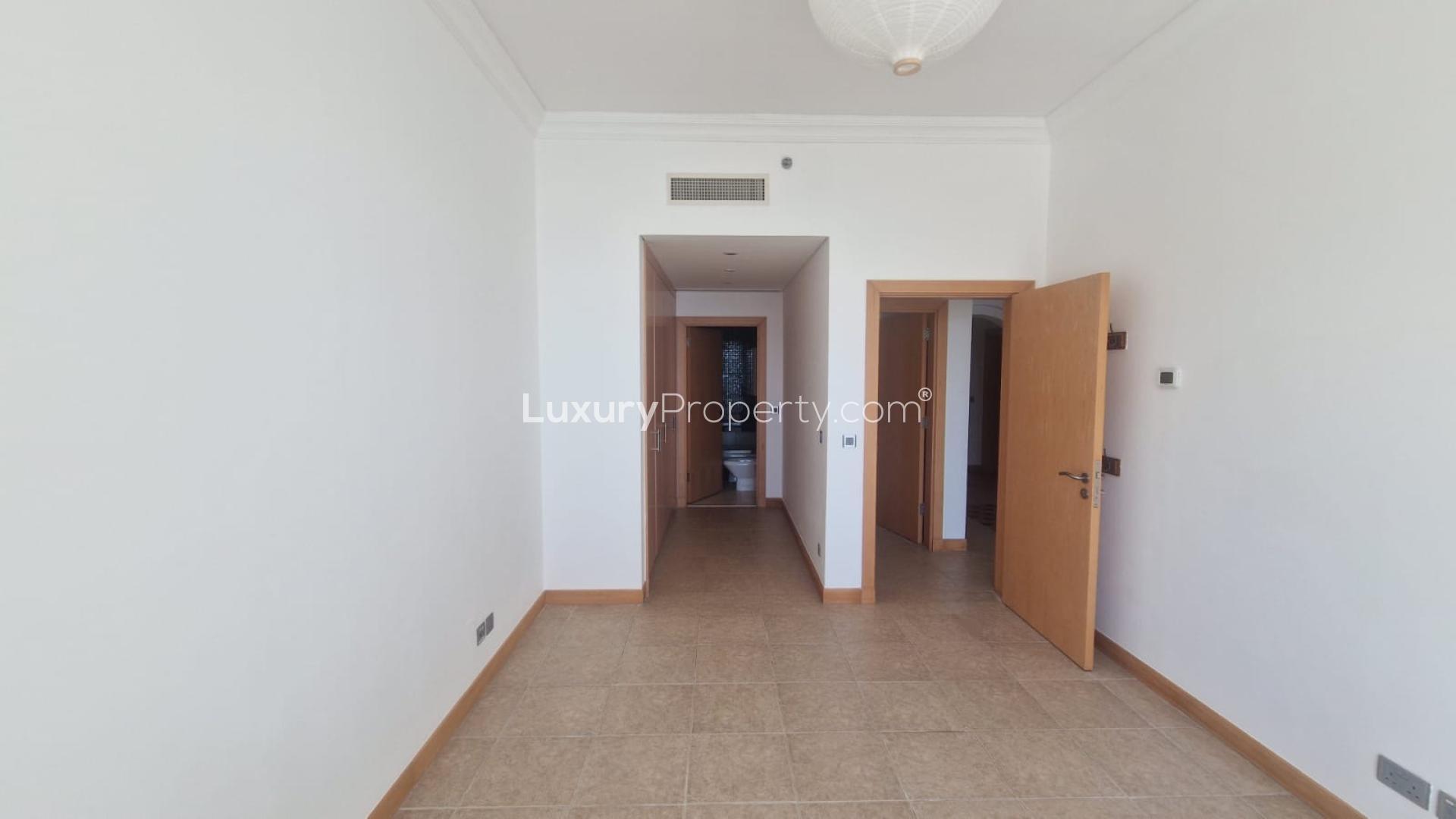 "Beachfront view from Shoreline Apartments, Palm Jumeirah, with lush greenery and sea vista.",Empty room view in Shoreline Apartments, Palm Jumeirah, featuring tiled floors and open doors