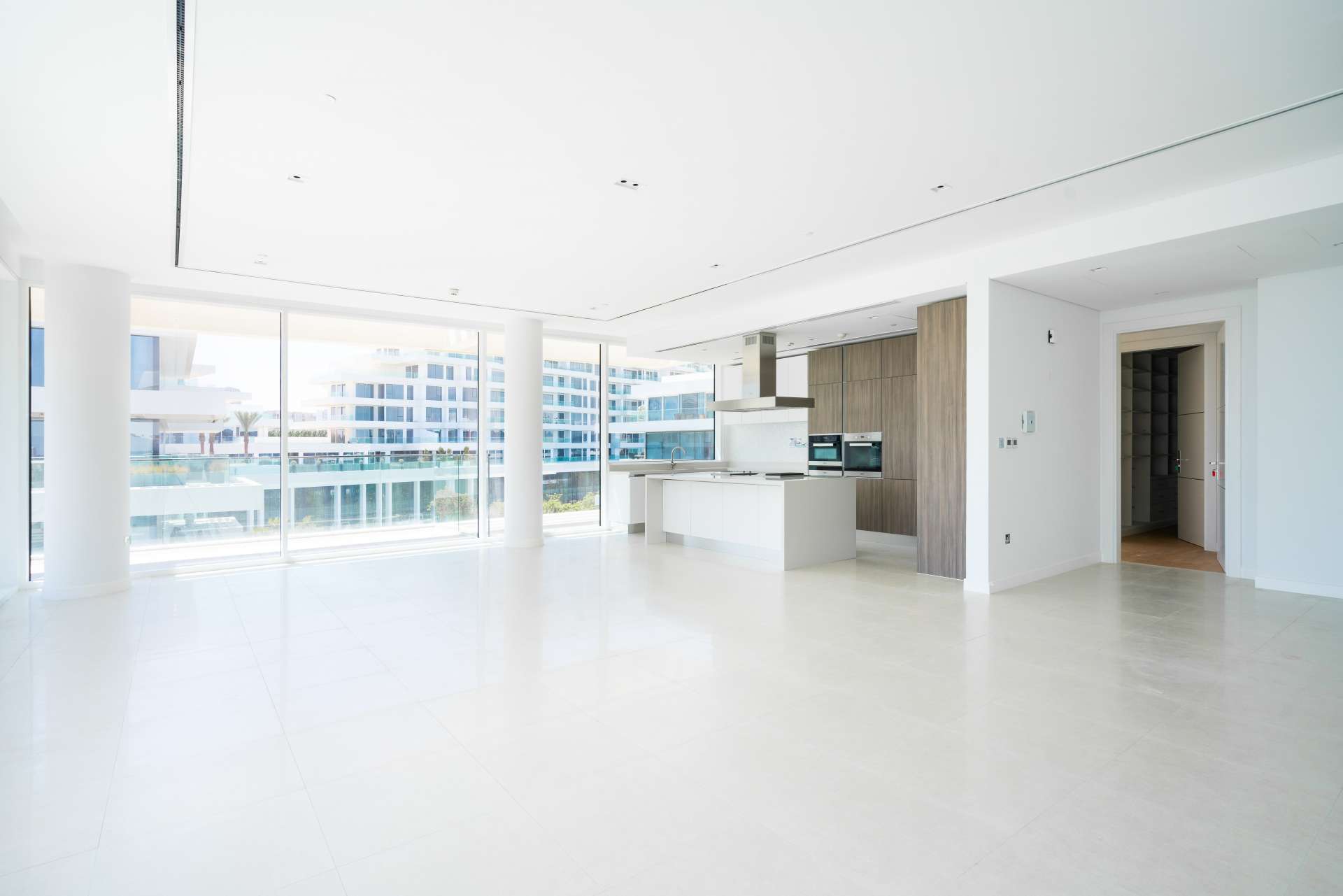 "Bright living room in 2-bedroom Ashjar apartment, Al Barari, with large windows and balcony view.",Modern open-plan kitchen and living area in Ashjar, Al Barari apartment for rent