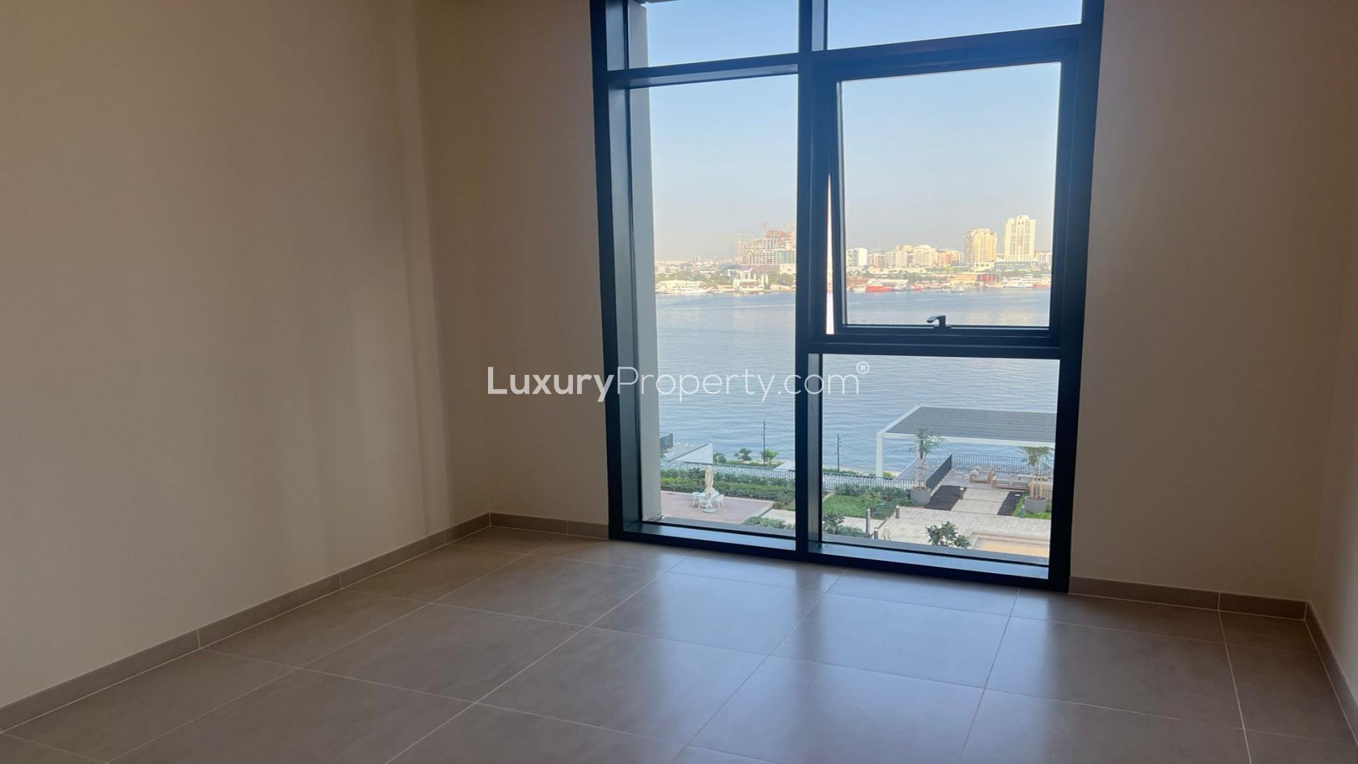 "Spacious living room with balcony view in Creek Edge apartment, Dubai Creek Harbour.","Bright apartment room with stunning Dubai Creek Harbour waterfront view through large window.",Built-in wooden closet in 2-bedroom apartment, Creek Edge, Dubai Creek Harbour