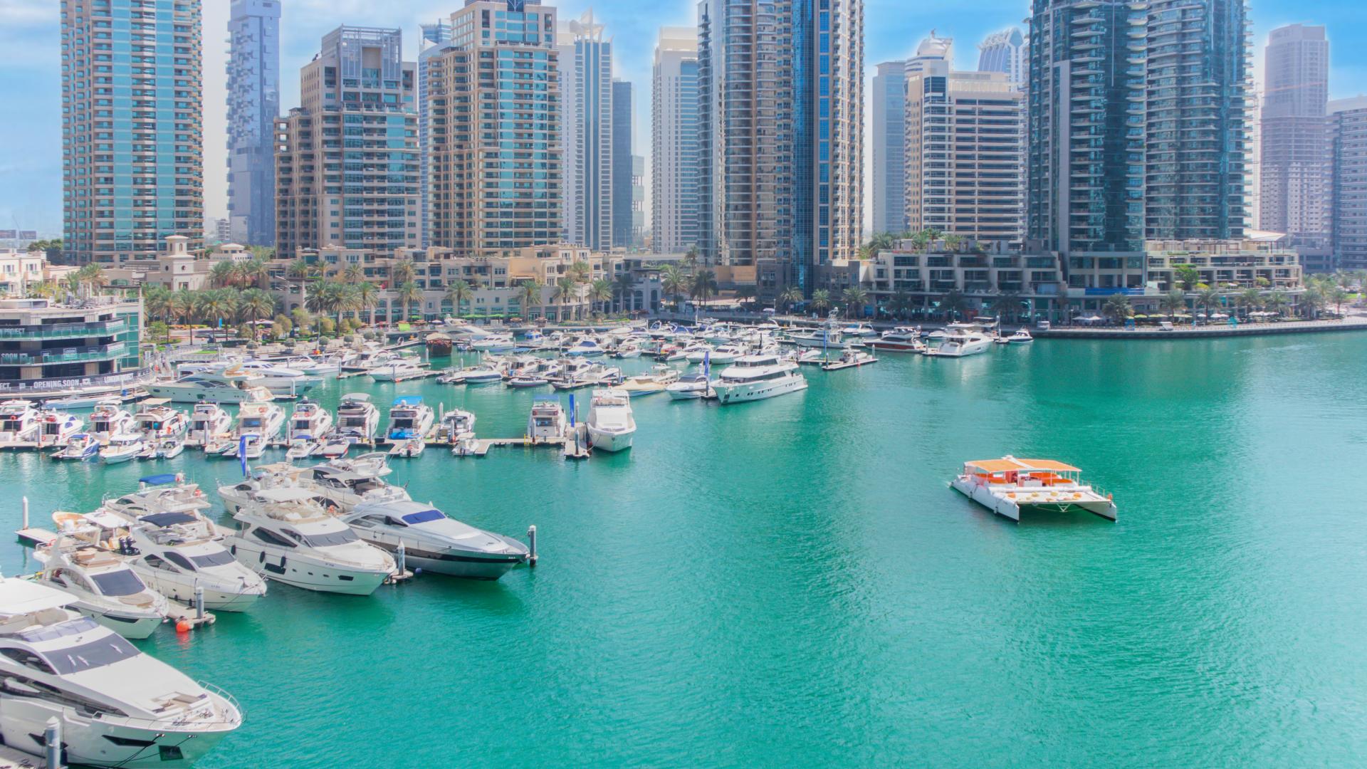 Alt text: "Cayan Tower exterior view, deluxe two-bedroom apartment for rent in Dubai Marina.",Dubai Marina view with yachts near Cayan Tower, deluxe two-bedroom apartment for rent