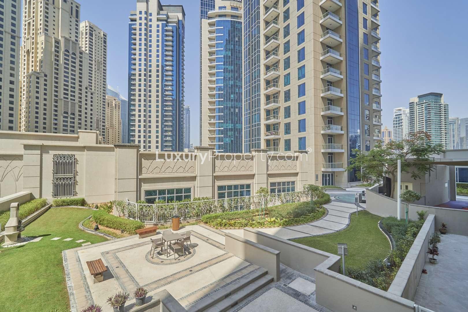 "Modern kitchen in spacious Marina Promenade apartment, granite countertops, wooden cabinets, Dubai Marina.",Exterior view of Marina Promenade apartment complex in Dubai Marina with garden area