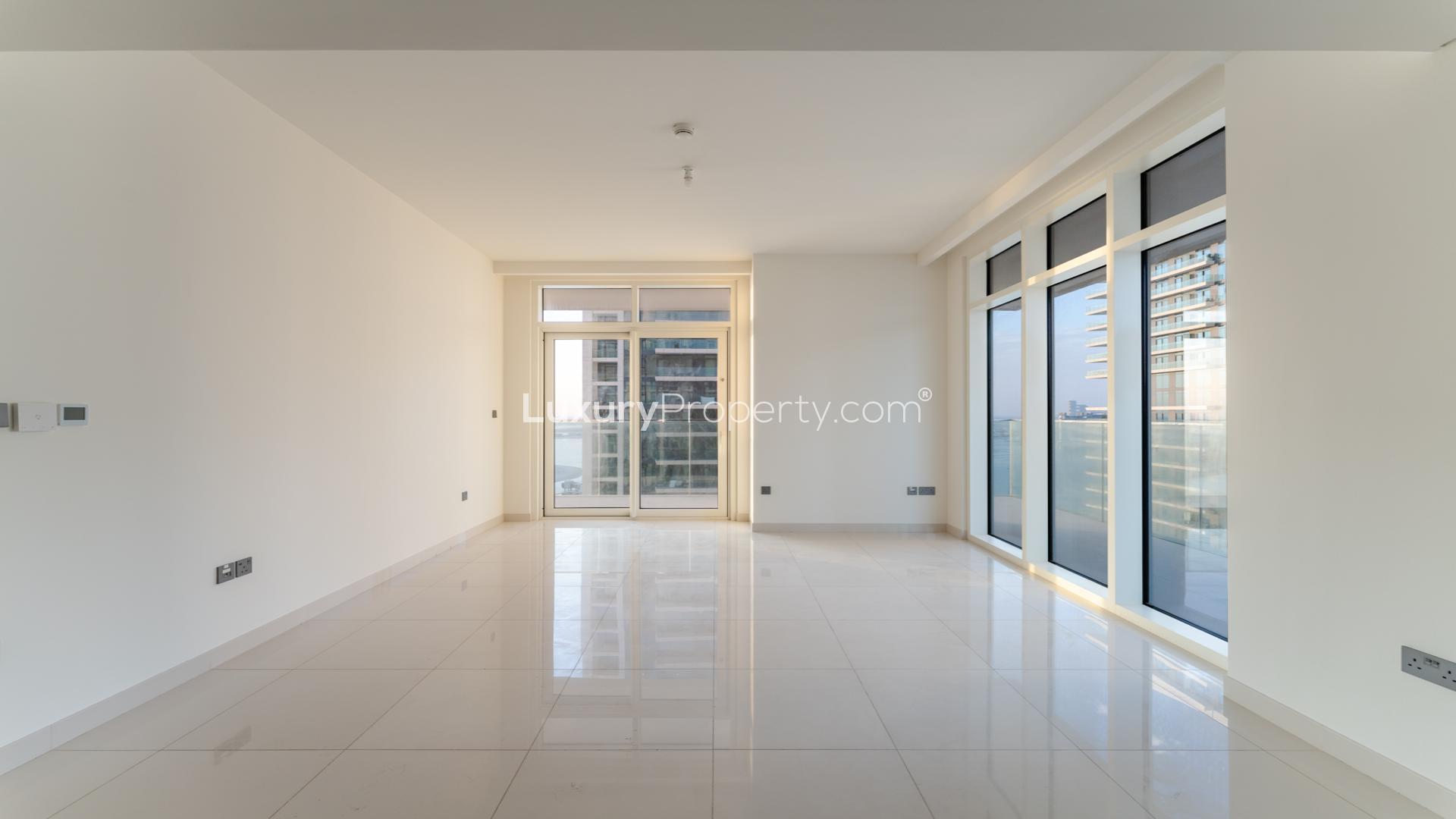 "Spacious balcony view in Emaar Beachfront apartment, Dubai Harbour, overlooking modern high-rise buildings.",Empty living room with large windows in Emaar Beachfront apartment, Dubai Harbour