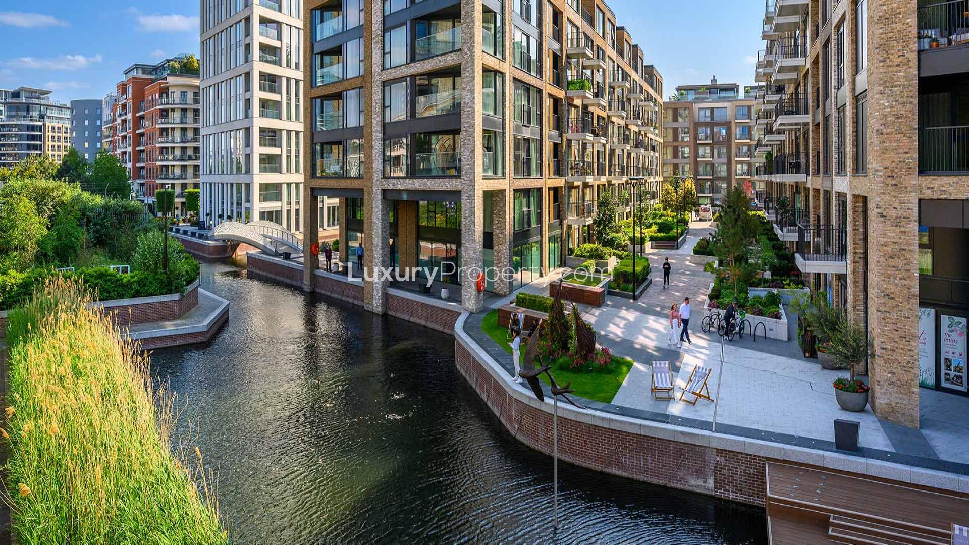 "Elegant Chelsea Creek apartment balcony with modern seating and garden view, London SW6 2FS.",Elegant Chelsea Creek apartment exterior with waterfront view, lush greenery, and modern architecture