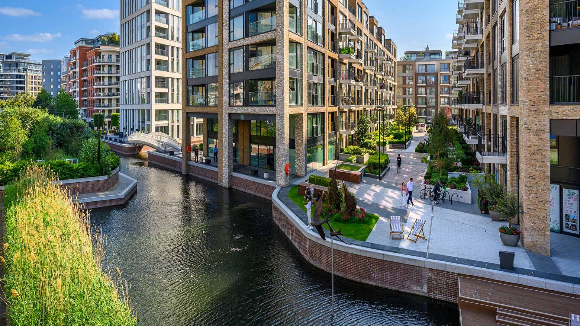 "Elegant Chelsea Creek apartment balcony with modern seating and garden view, London SW6 2FS.",Elegant Chelsea Creek apartment exterior with waterfront view, lush greenery, and modern architecture
