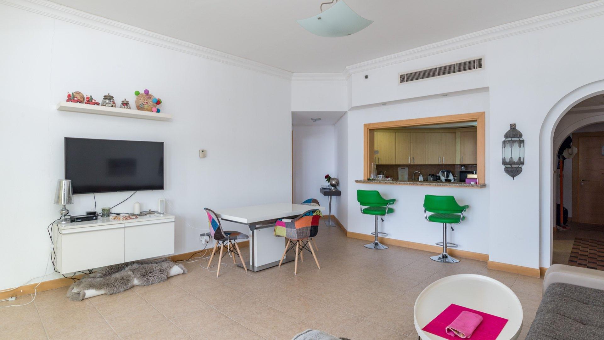 "Modern kitchen in Palm Jumeirah apartment with granite countertops and sea view window.",Modern living room in Shoreline Apartments, Palm Jumeirah, with open kitchen and colorful chairs