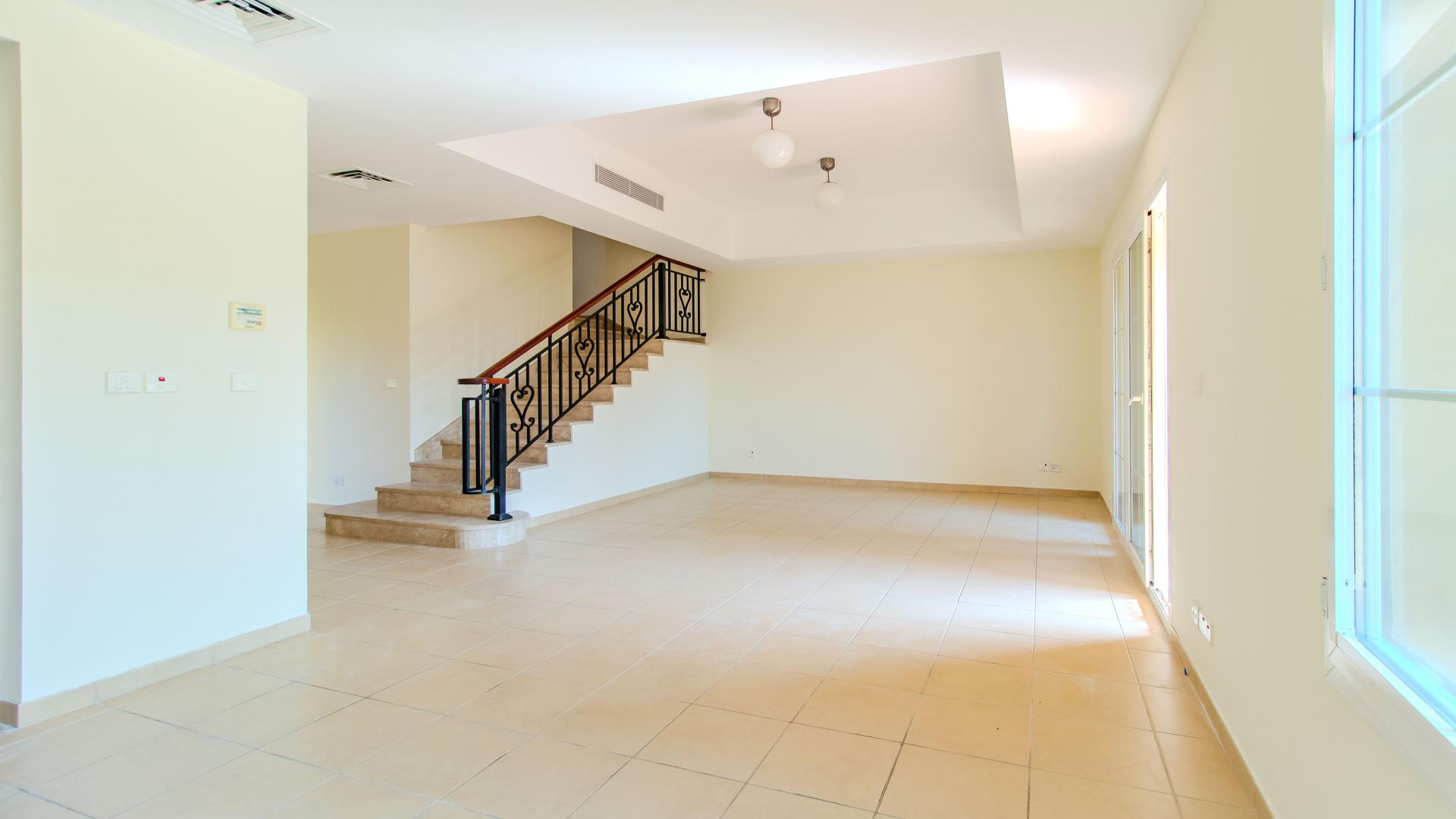 "Spacious kitchen with wooden cabinets in Palmera villa, Arabian Ranches, available for rent.",Bright living room in well-maintained Palmera villa, Arabian Ranches, with staircase and tile flooring