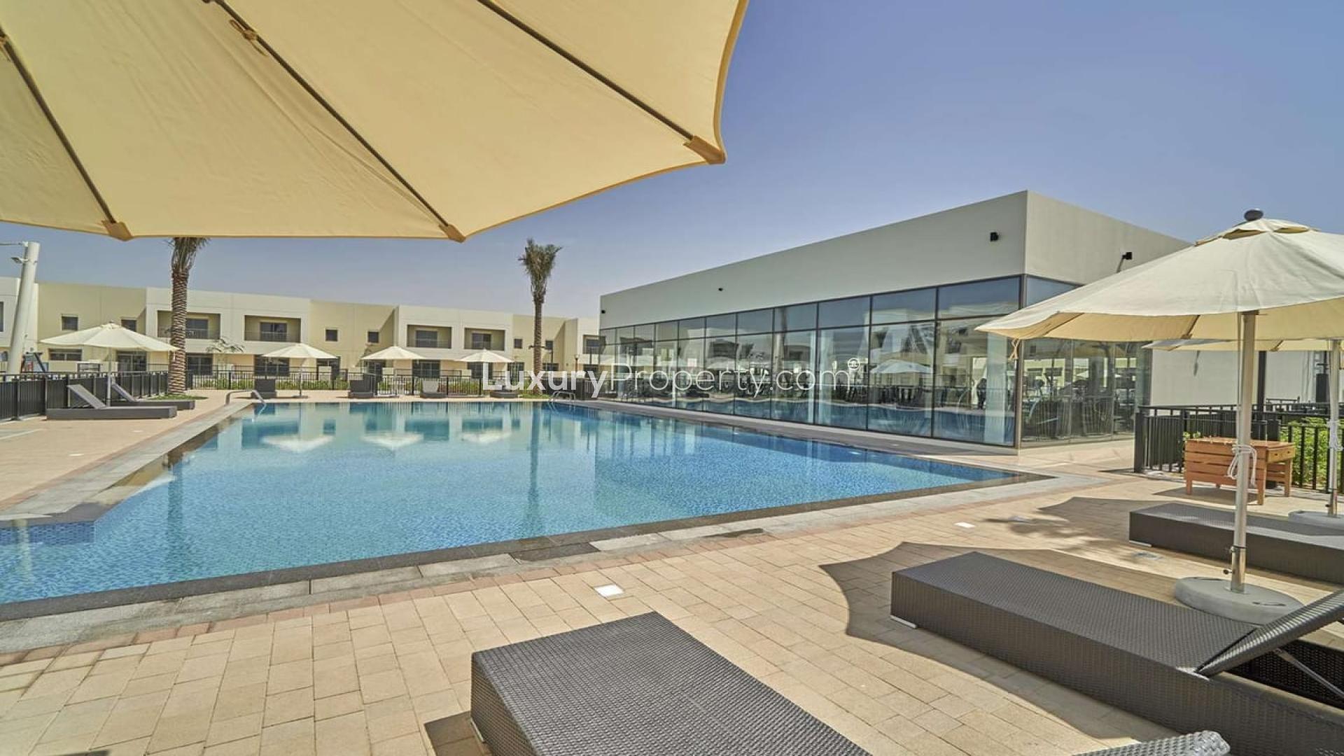 Outdoor pool area at Naseem Townhouses, Town Square, with sun loungers and umbrellas