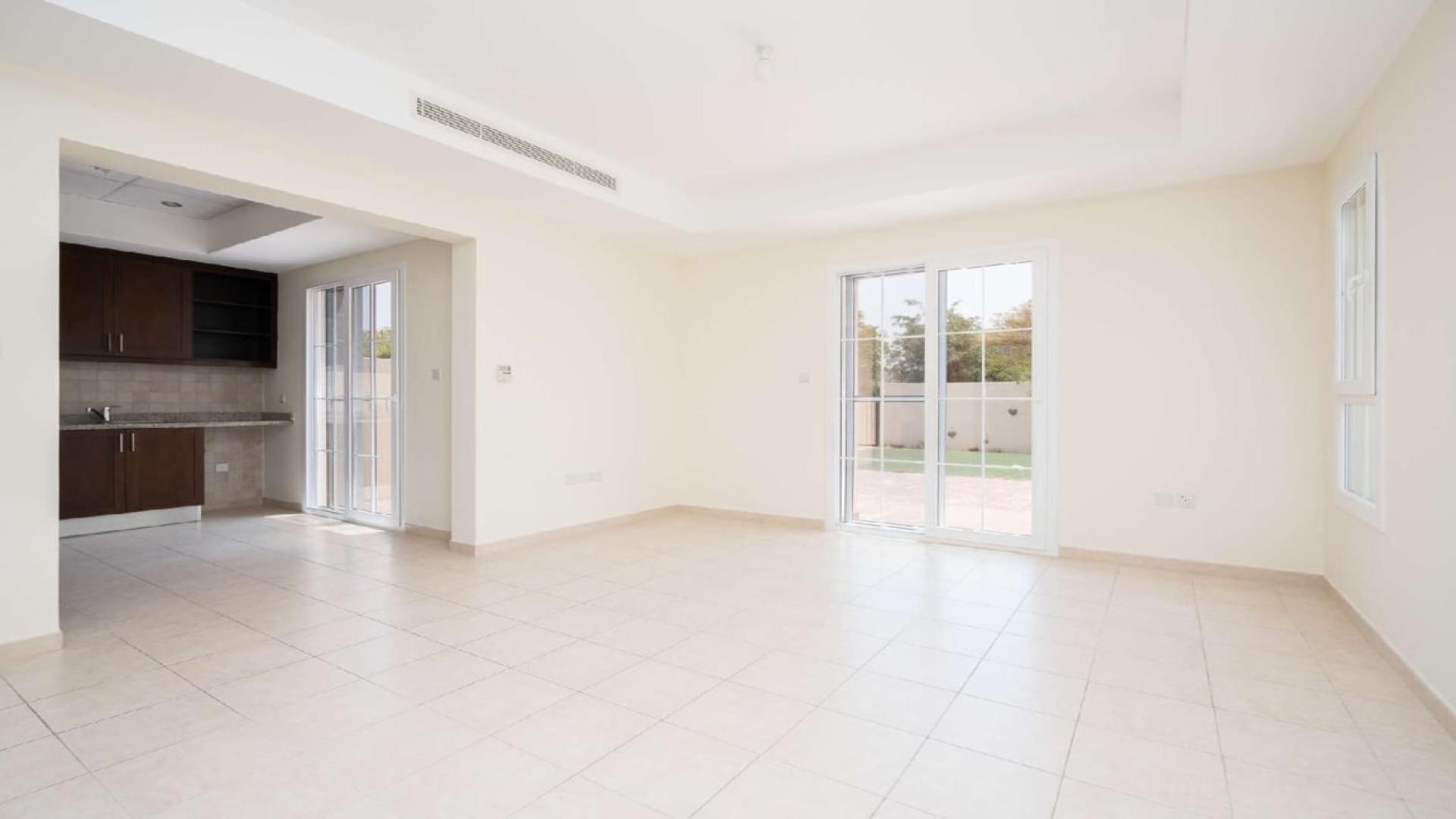 Spacious living area with built-in shelves and open kitchen in Alma villa, Arabian Ranches