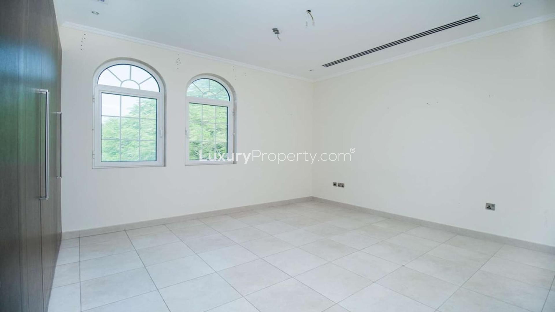 "Charming Legacy villa entrance with lush garden in Jumeirah Park, Dubai, for rent.",Empty bedroom with tiled floor and arched windows in Jumeirah Park villa for rent