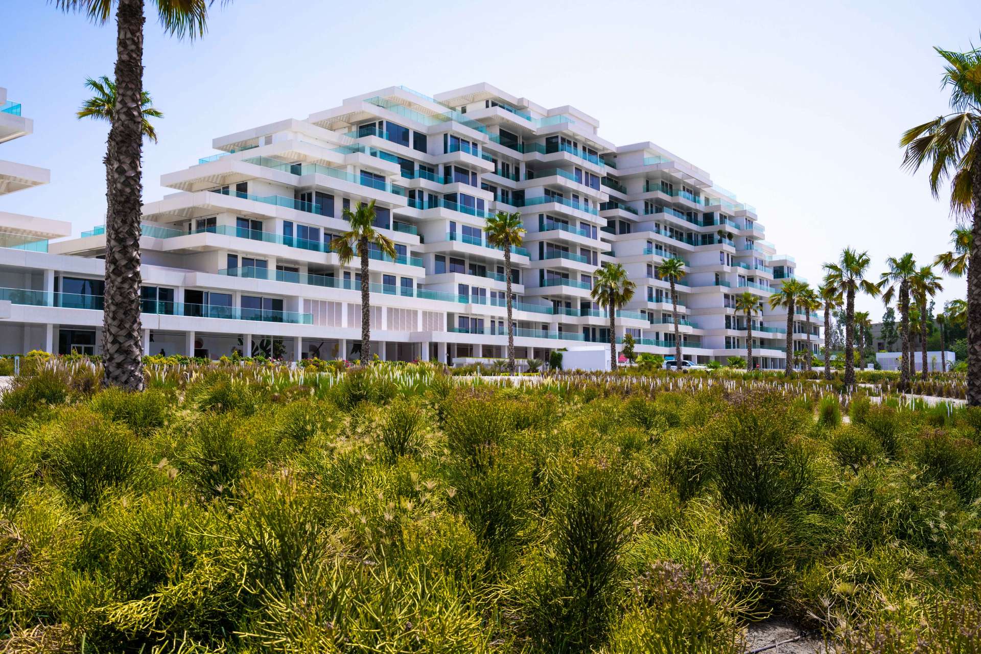 "Modern white apartment complex in Seventh Heaven, Al Barari, surrounded by palm trees and greenery.","Modern apartment complex in lush surroundings, Seventh Heaven, Al Barari, available for rent.",Spacious living area with large windows in Seventh Heaven, Al Barari apartment for rent