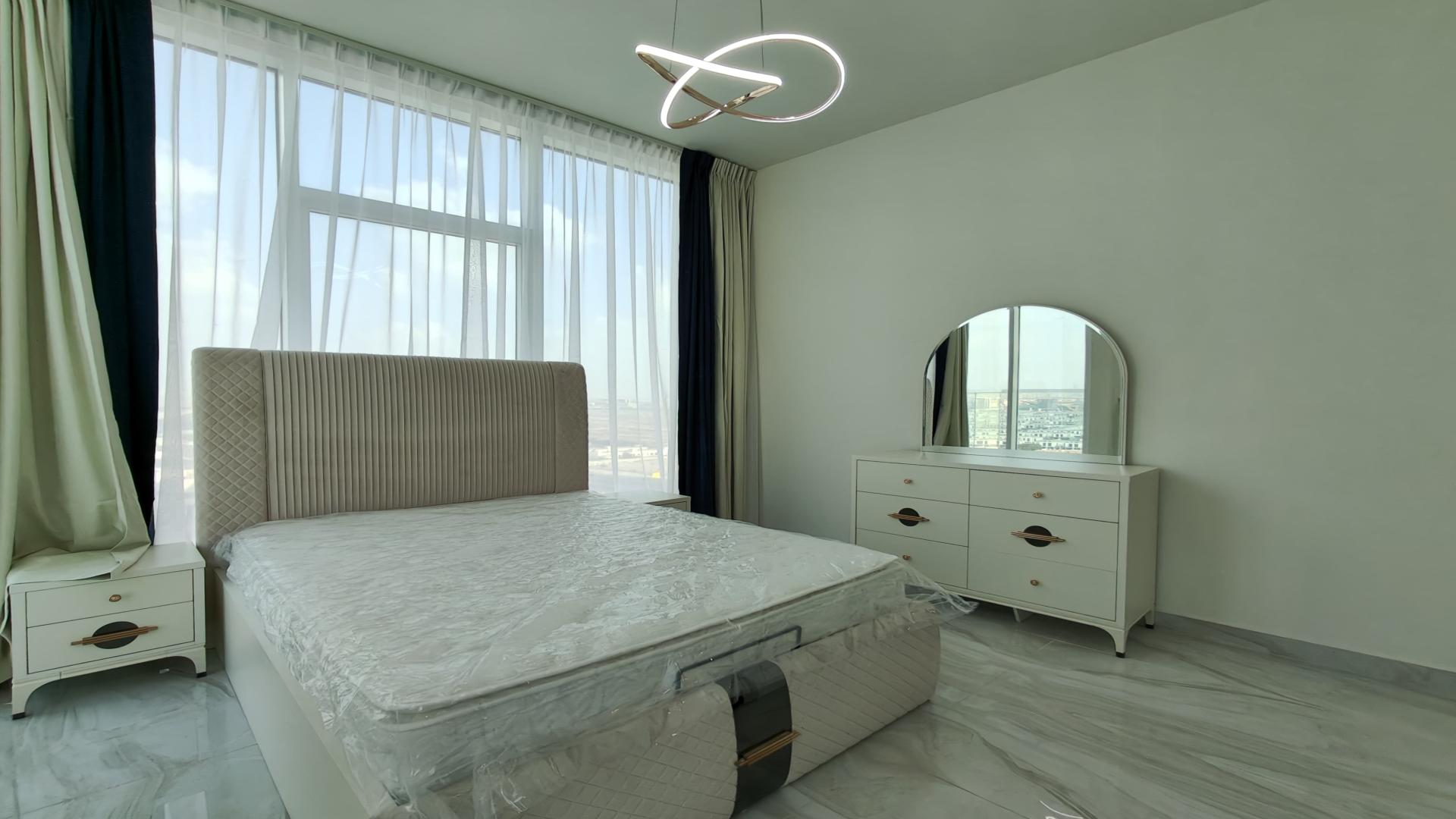 Modern bedroom in Al Furjan penthouse, featuring elegant bed and dresser with city view