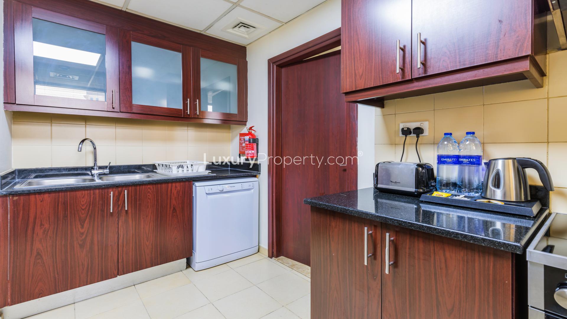 Modern kitchen in fully furnished JBR apartment, featuring wood cabinets and appliances
