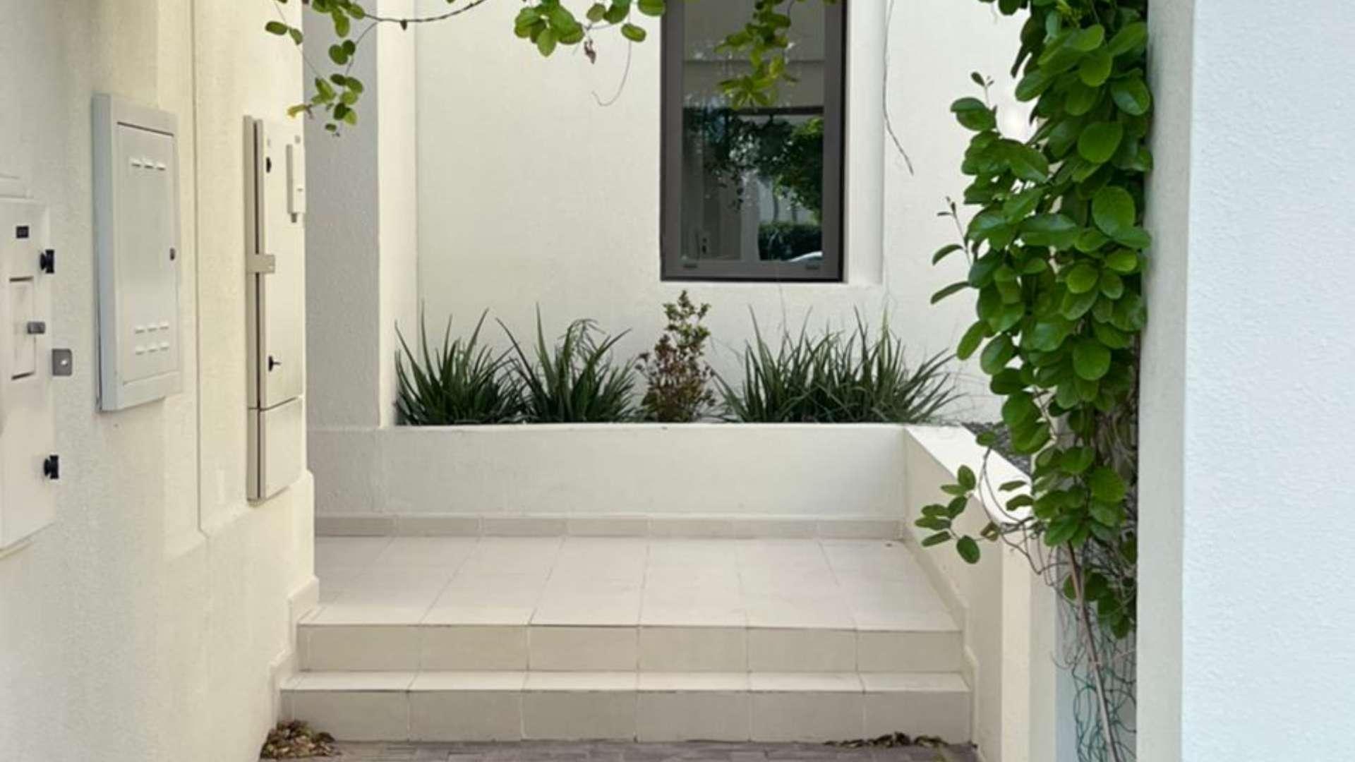 "Backyard view of Mira Oasis townhouse for rent, featuring lush garden and modern facade.",Entrance of Mira Oasis townhouse with greenery and modern design in Reem community