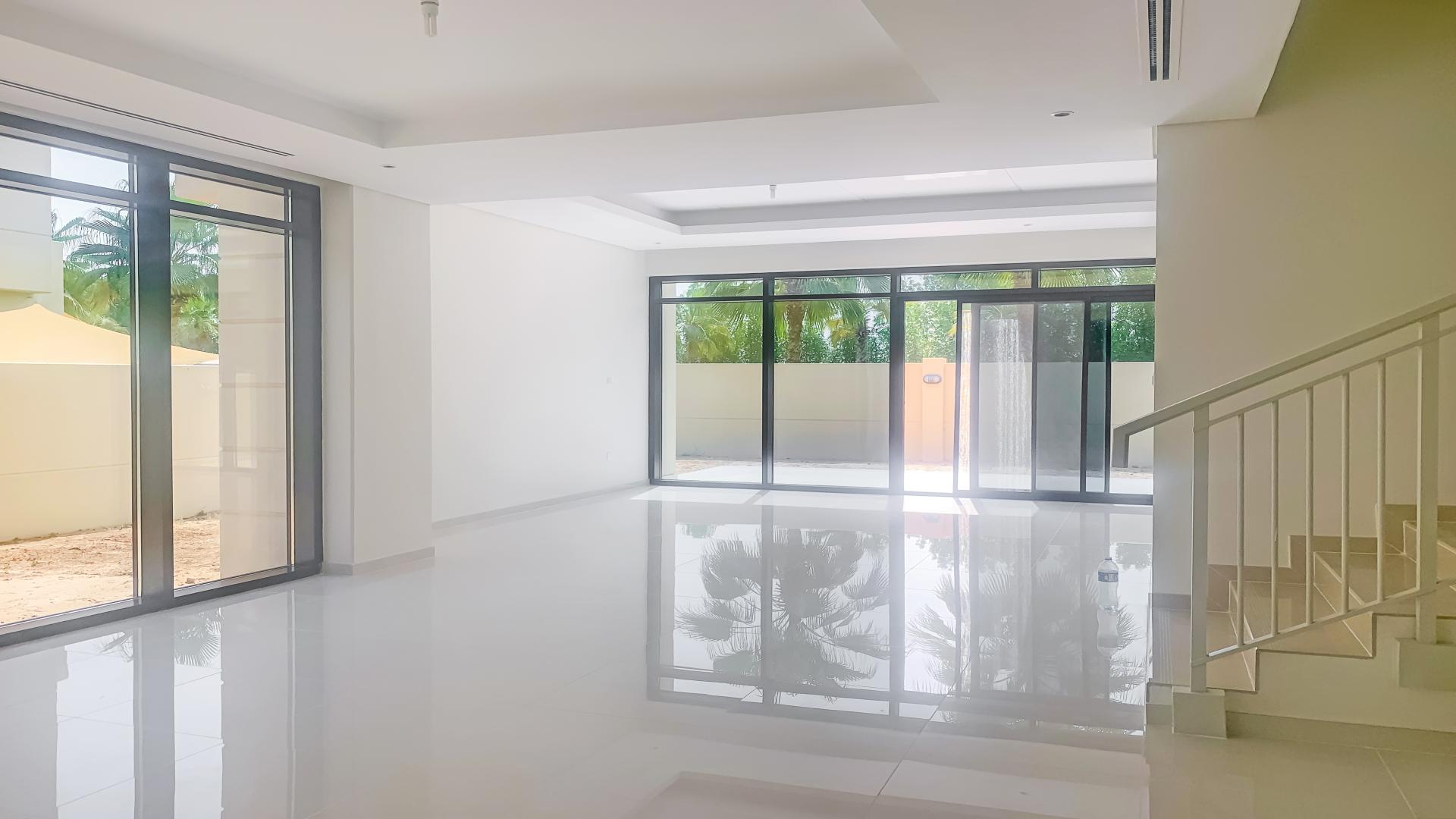 "Bright room with large windows overlooking greenery in Damac Hills townhouse, Queens Meadow.",Spacious living area with large windows in Damac Hills townhouse for rent