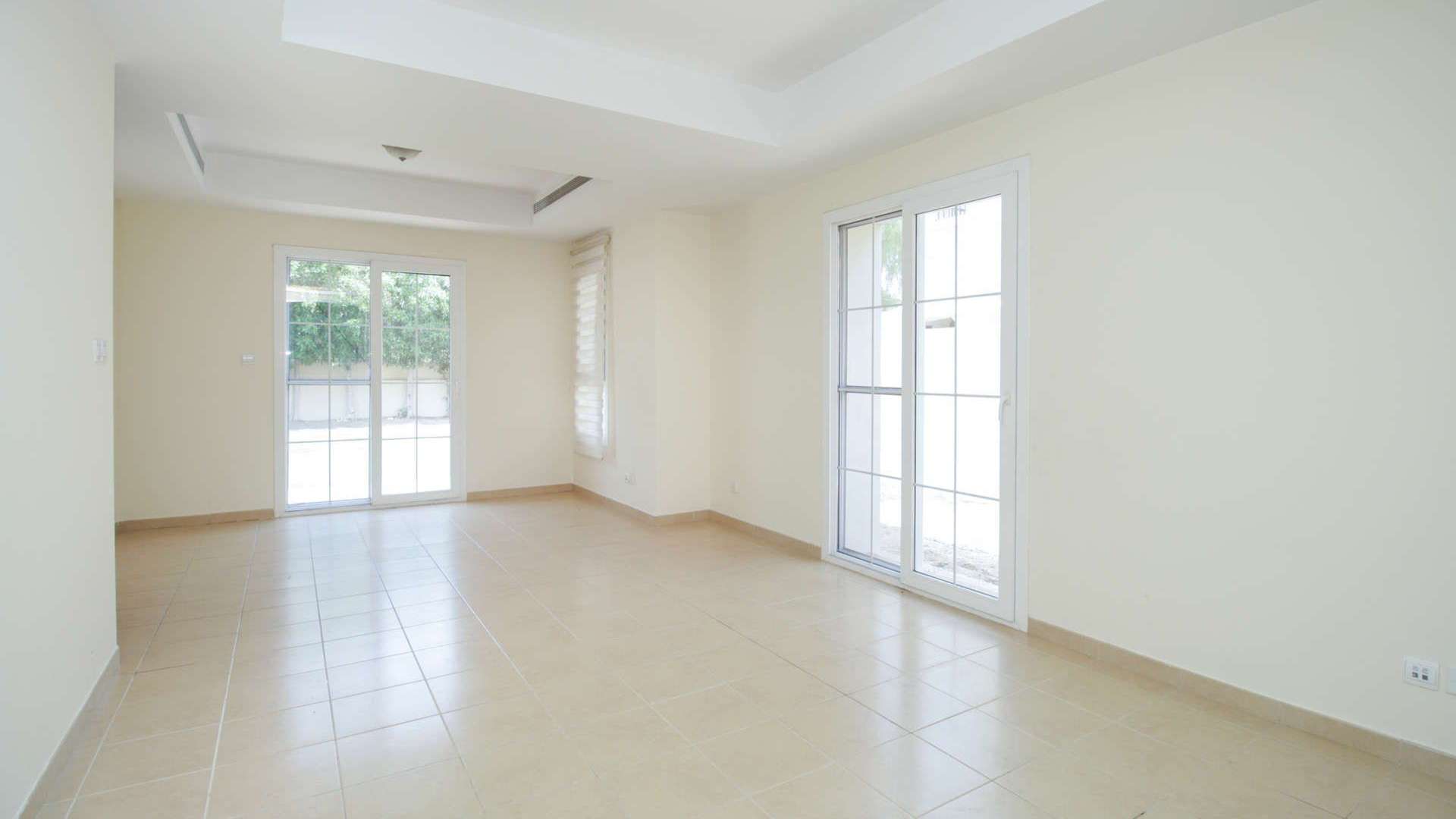 Bright living area in vacant Arabian Ranches townhouse, featuring large windows and tile flooring