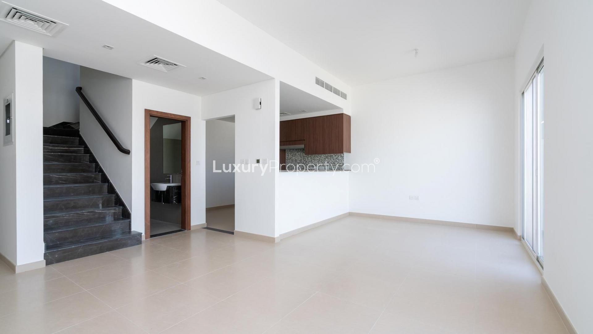 "Bright empty room in Arabella 3 townhouse, Mudon with large window and tiled floor.",Open-plan living area in 3-bedroom townhouse, Arabella 3, Mudon, with modern staircase and kitchen