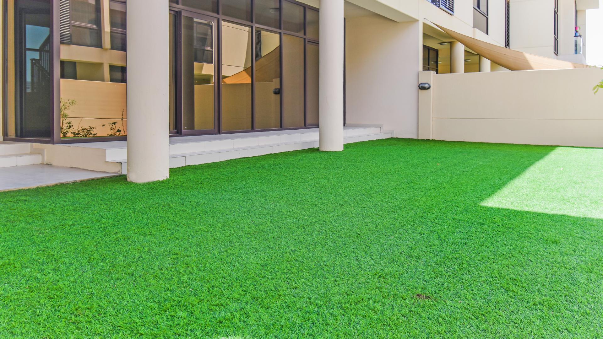 Outdoor patio area with green artificial lawn in Akoya Park villa, Damac Hills