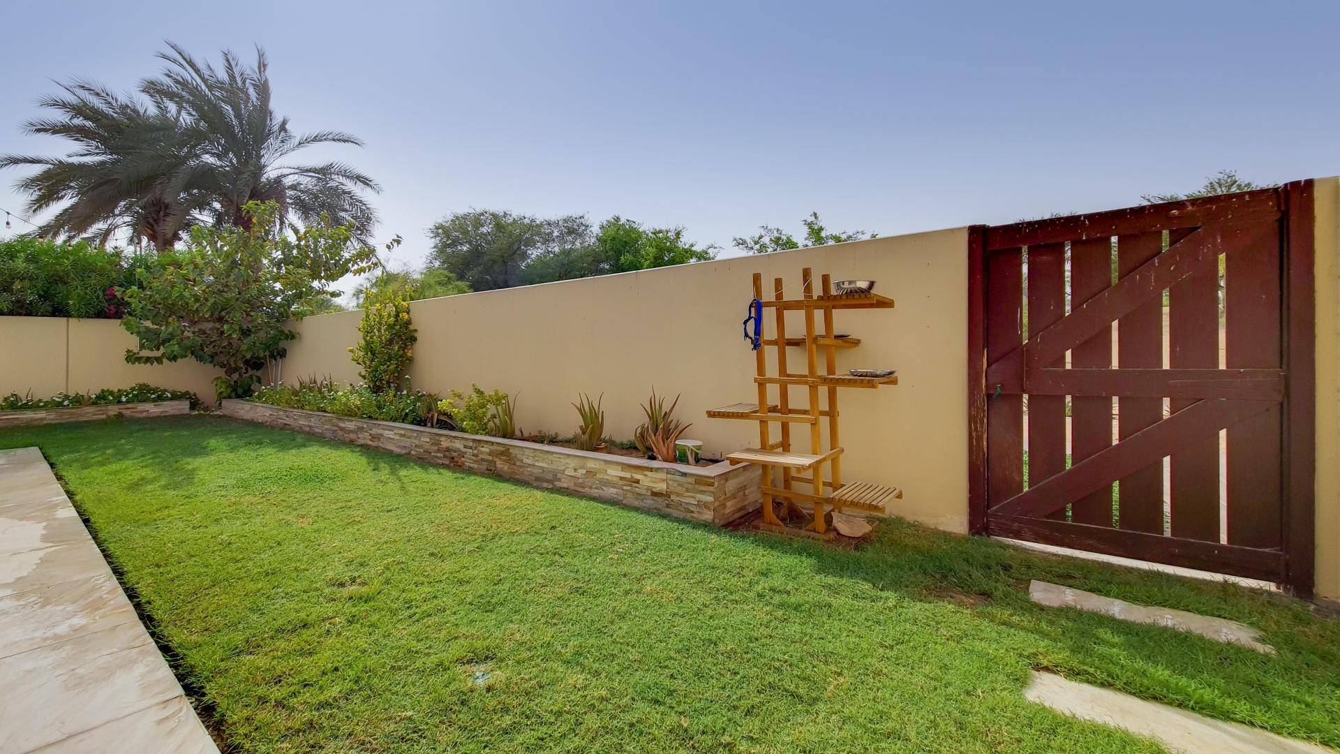 Alt text: "Scenic view from Type 2E villa in Al Reem, Arabian Ranches with lush greenery.",Sunny garden view in Al Reem villa, Arabian Ranches, with lush greenery and wooden gate
