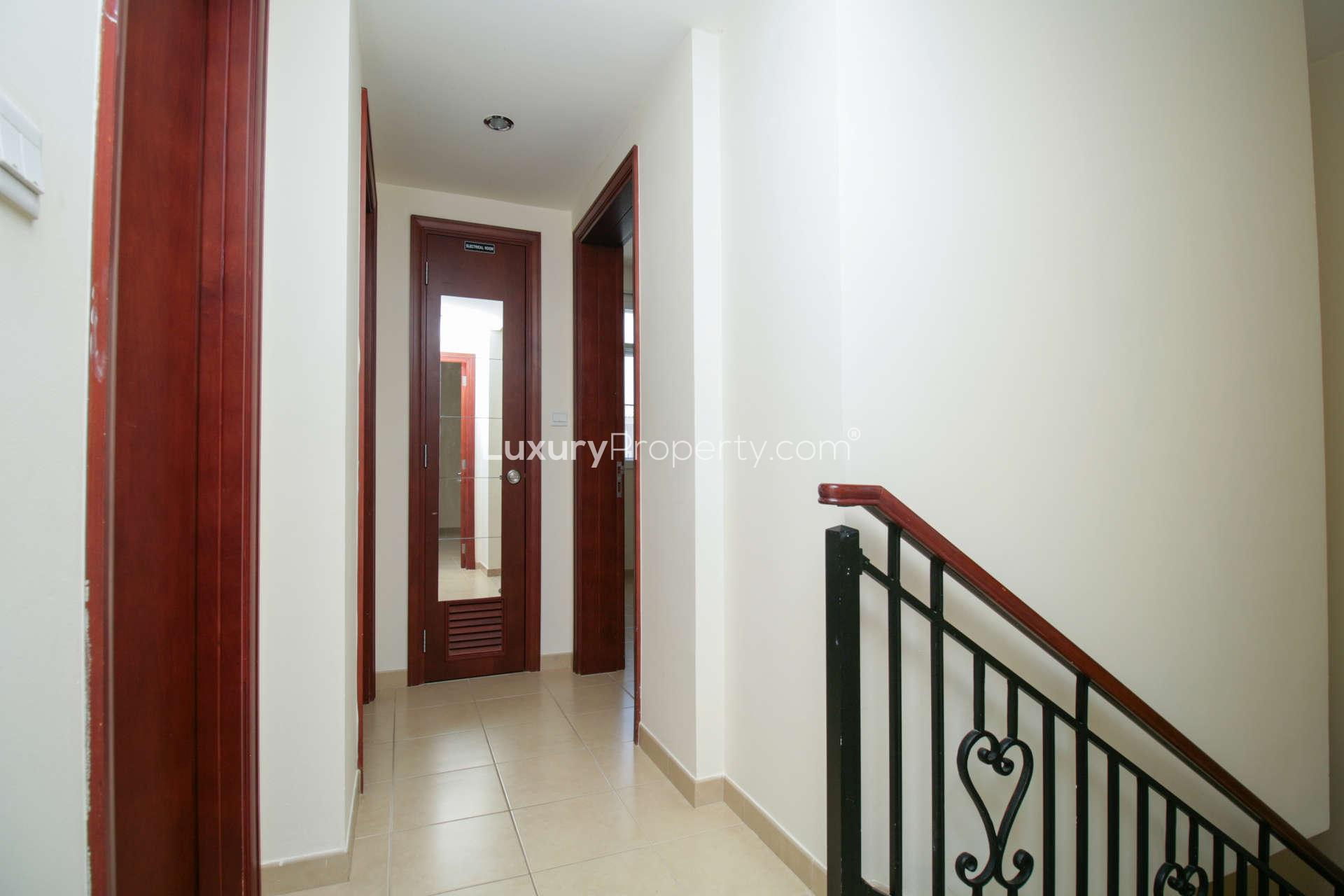 "Spacious kitchen with wooden cabinets in 3-bedroom villa, Alma, Arabian Ranches, for rent.",Hallway with wooden doors and staircase in Alma, Arabian Ranches villa for rent