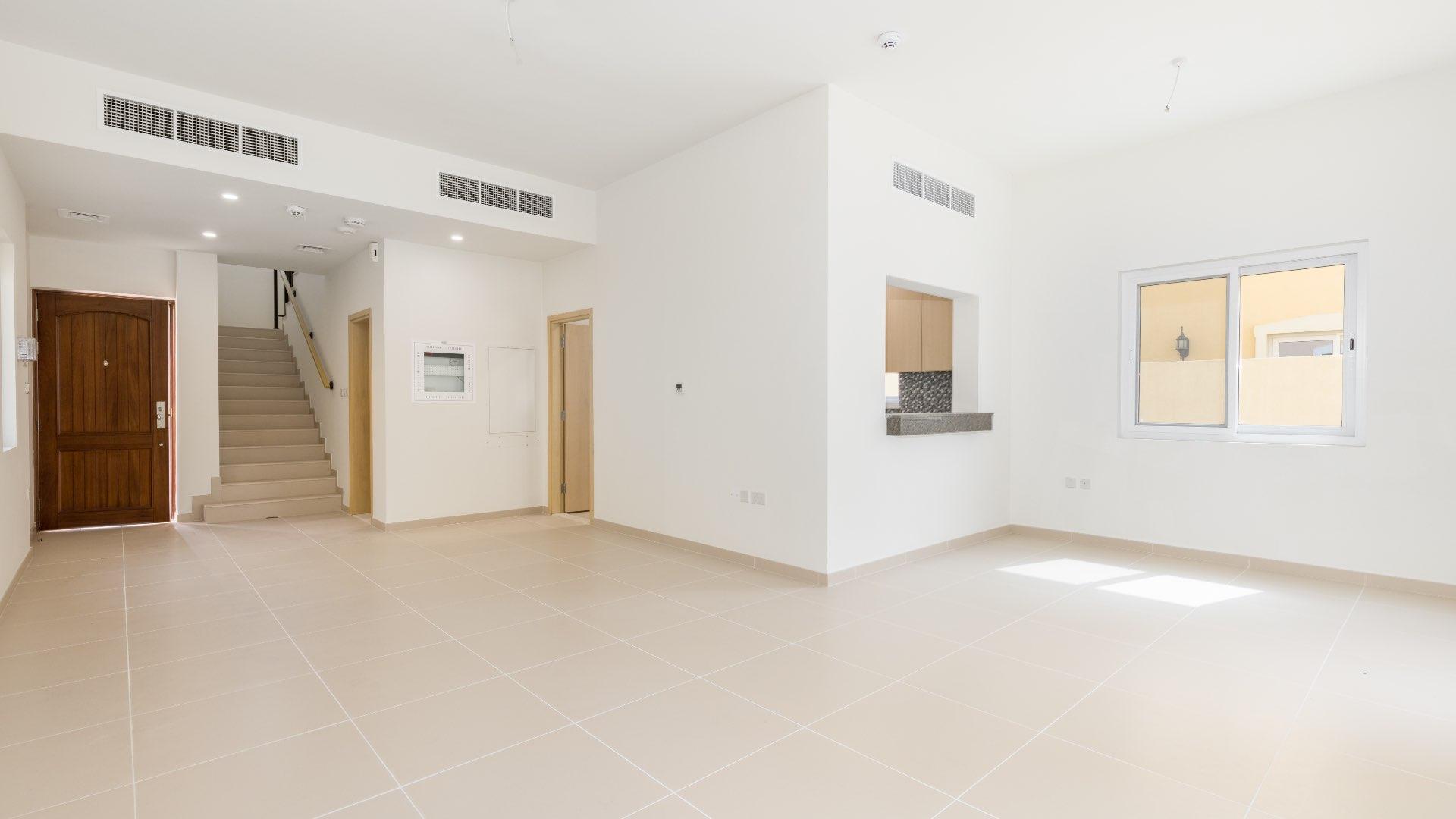 Bright living room in Villanova villa, Dubai Land, with kitchen view and patio access