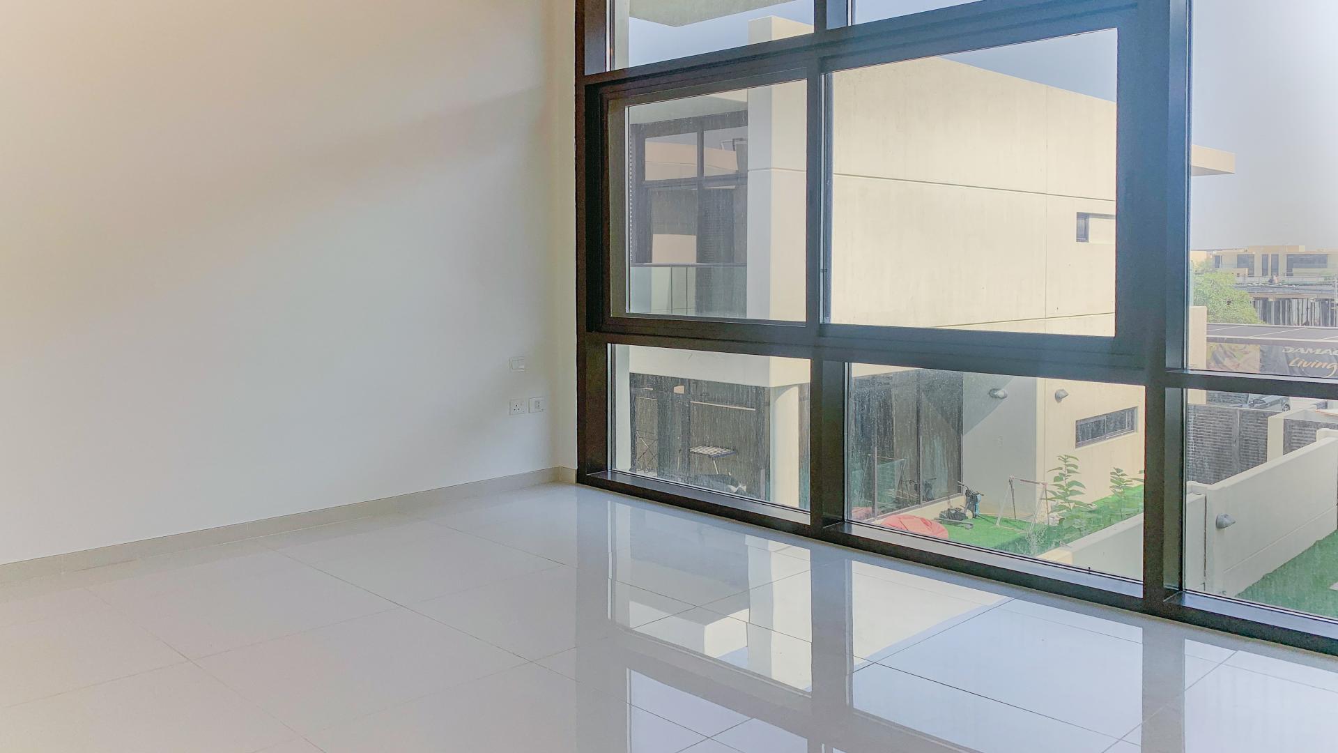 "Bright living room in modern Damac Hills villa for rent, spacious windows, LP13593.",Modern villa interior with large windows overlooking Rochester community in Damac Hills