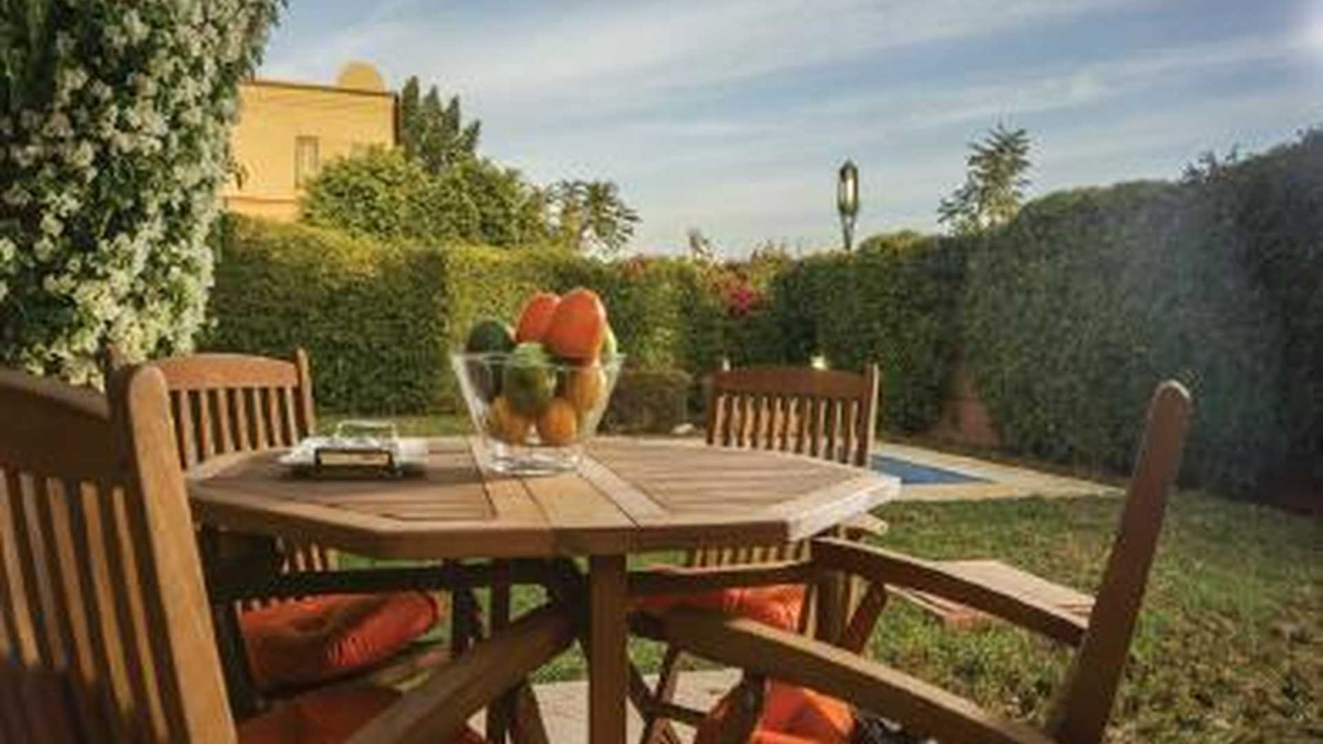 Outdoor patio with wooden table and chairs, villa garden view, Amelkis Resorts Marrakech