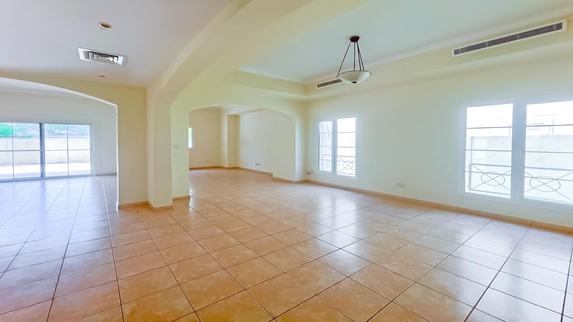 "Type 5 villa exterior in Deema, The Lakes, with patio and garden, for sale.",Spacious living area in Type 5 Villa, Deema, The Lakes, featuring tiled floors and large windows