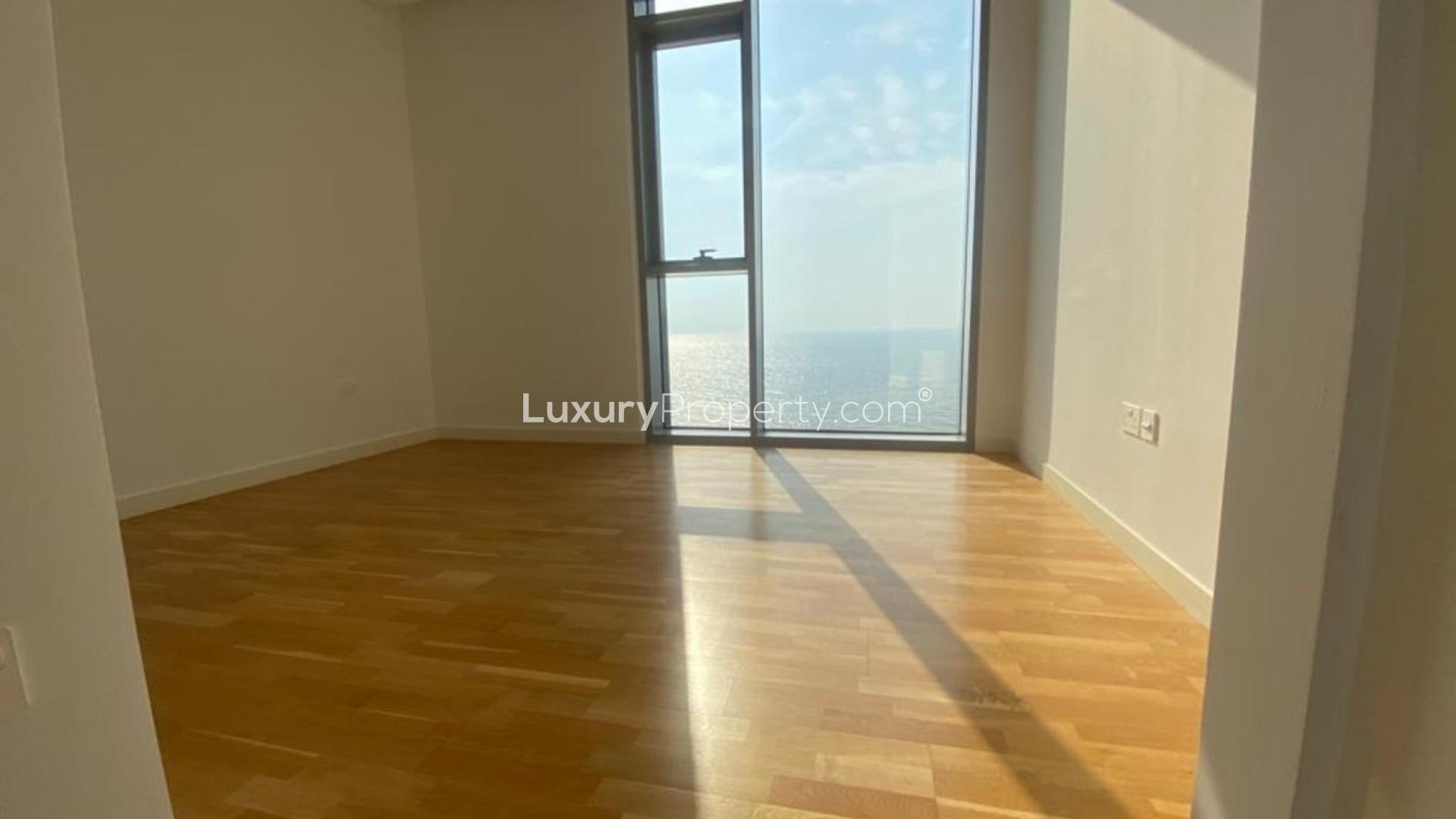 "Luxurious Bluewaters Residences apartment with sea view, modern architecture, and lush surroundings for sale.",Empty sunlit room with ocean view in Bluewaters Residences apartment, hardwood floors visible