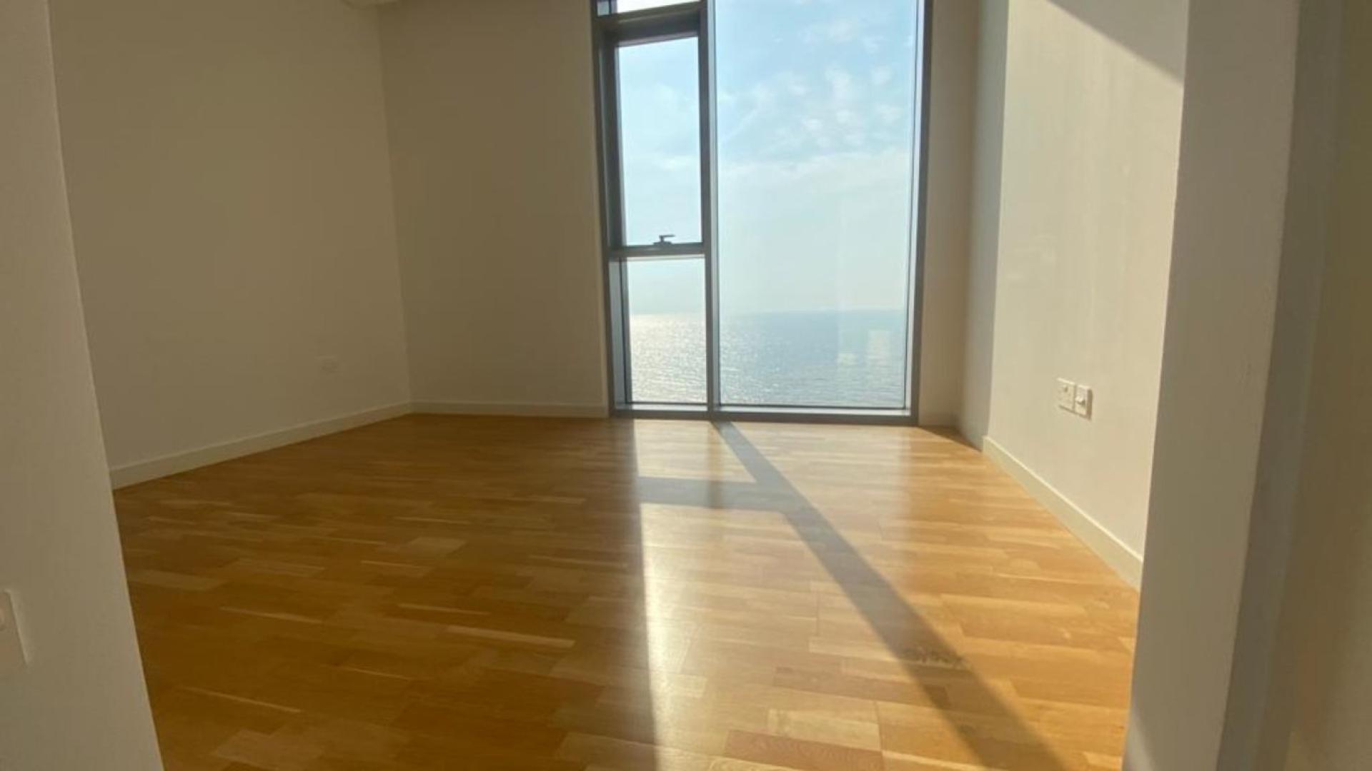 "Luxurious Bluewaters Residences apartment with sea view, modern architecture, and lush surroundings for sale.",Empty sunlit room with ocean view in Bluewaters Residences apartment, hardwood floors visible