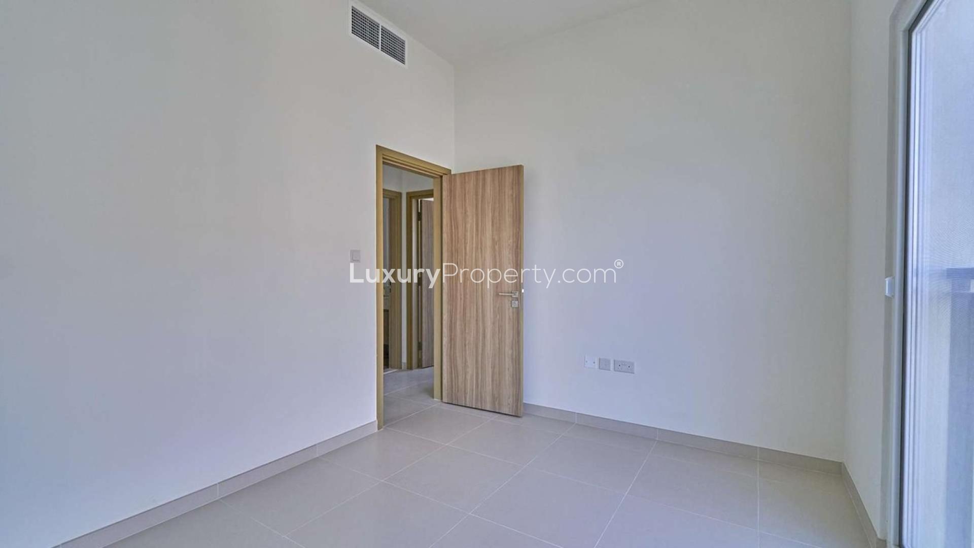 Alt text: "Vastu-compliant townhouse near pool in Villanova, Dubai Land, for sale, 4 bedrooms.",Empty room in Vastu-compliant townhouse, Dubai Land Villanova, featuring wooden door and window