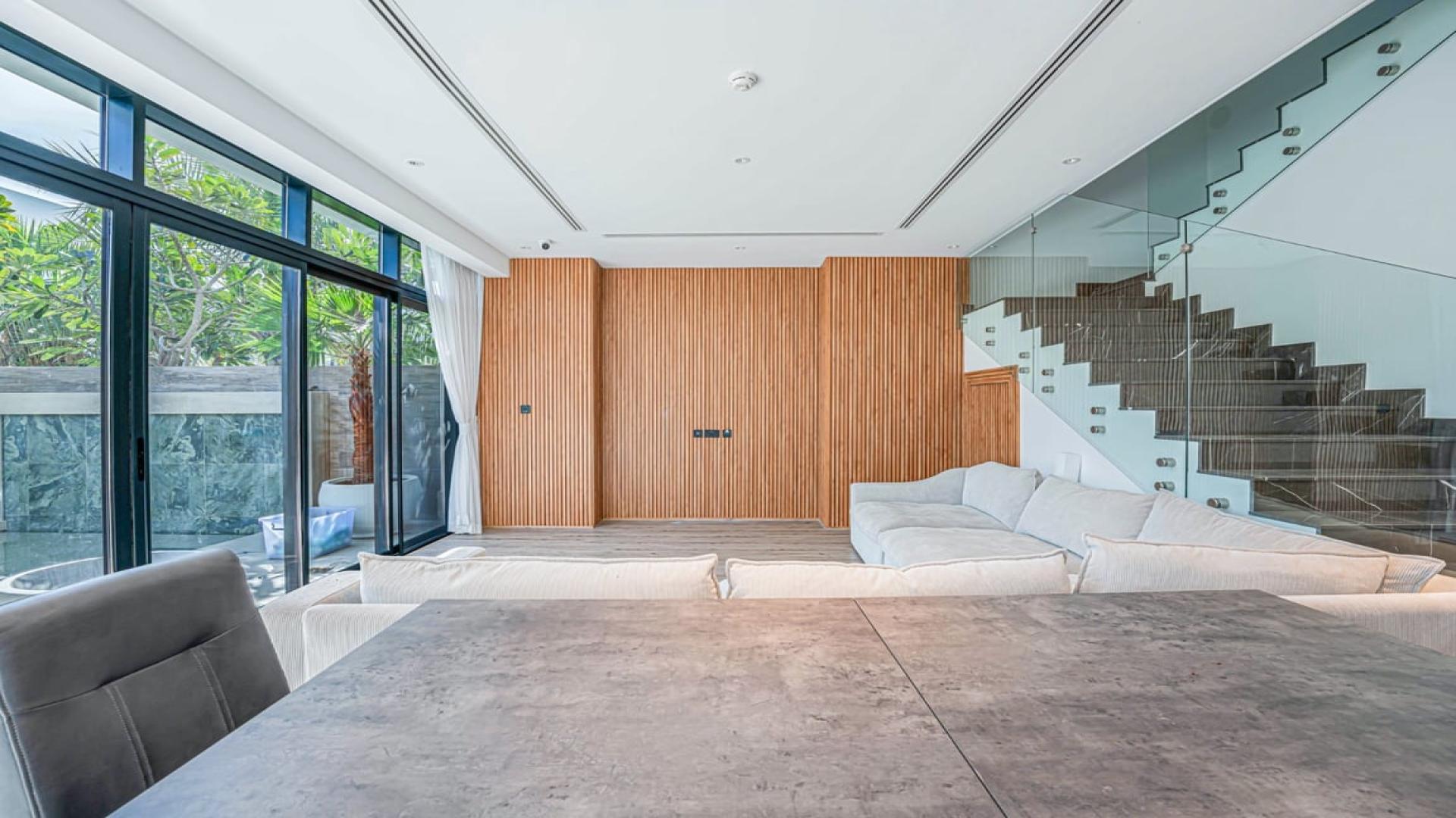 Contemporary villa living room with spacious sofa, open kitchen, and glass staircase in Jumeirah Luxury
