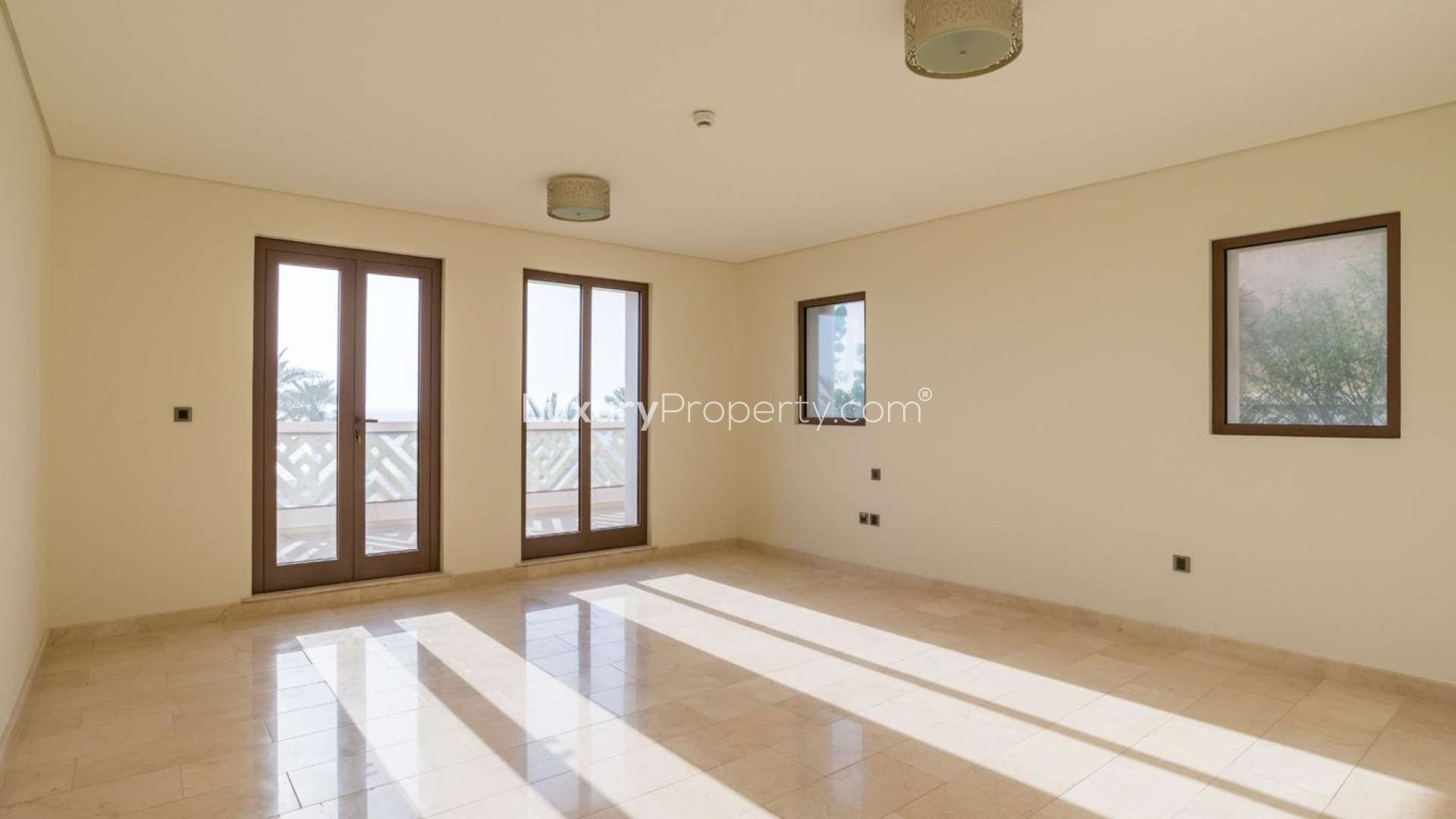 "Elegant villa exterior in Kingdom of Sheba, Palm Jumeirah, with garage and stone facade.",Empty sunlit room in Palm Jumeirah villa, featuring large windows and tiled floor