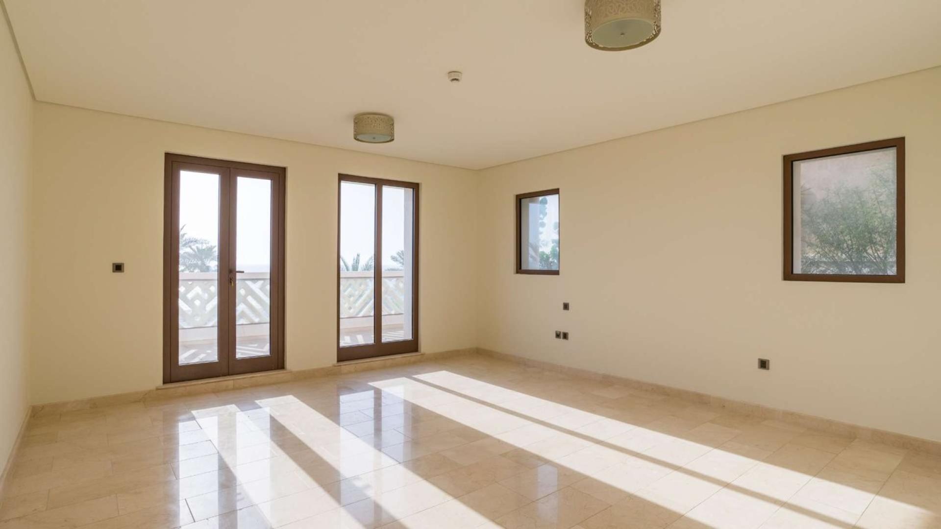 "Elegant villa exterior in Kingdom of Sheba, Palm Jumeirah, with garage and stone facade.",Empty sunlit room in Palm Jumeirah villa, featuring large windows and tiled floor